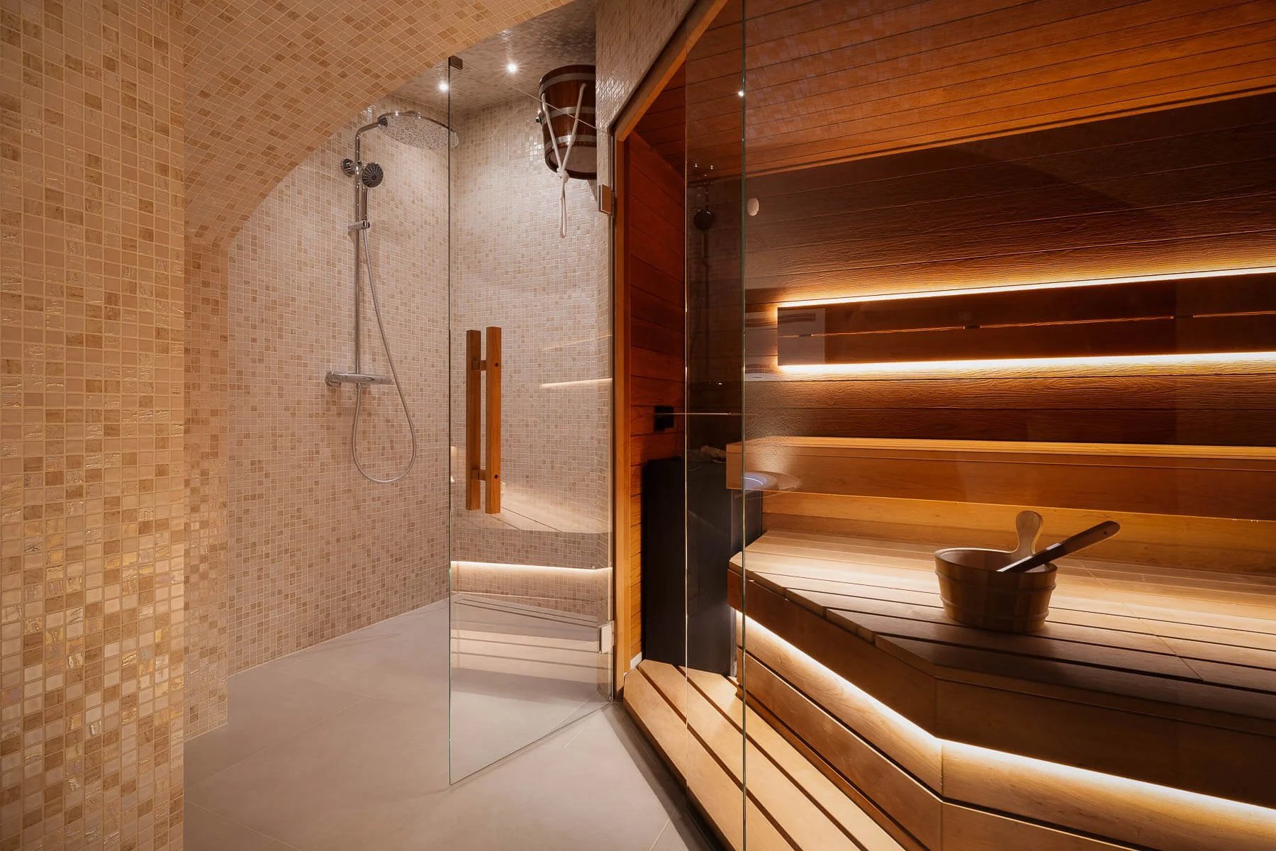 Designový wellness interiér s prosklenou sprchou, dřevěnou saunou a ambientním osvětlením.