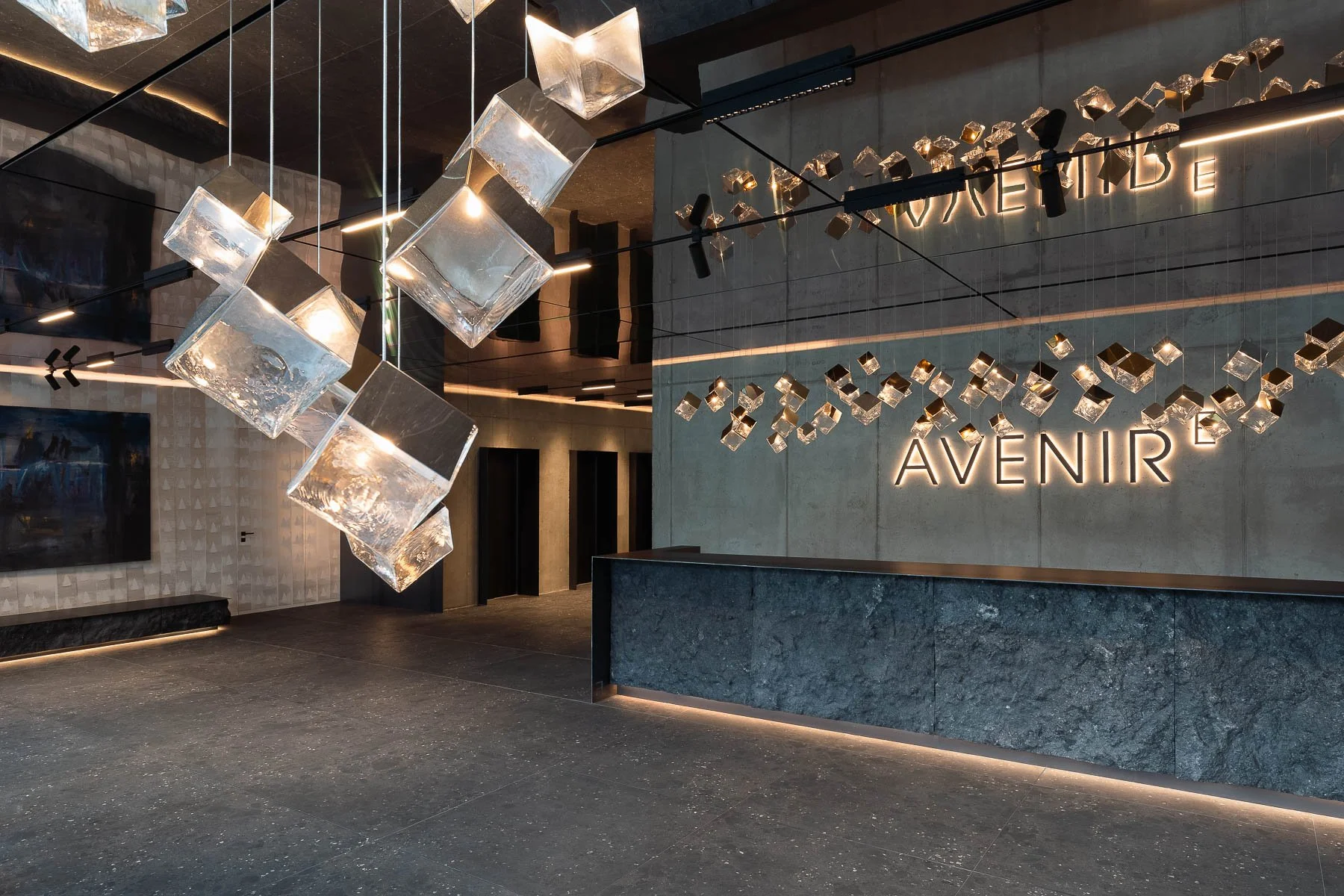 Moderní recepce hotelu s velkým kamenným pultem a geometrickými svítidly Bomma.