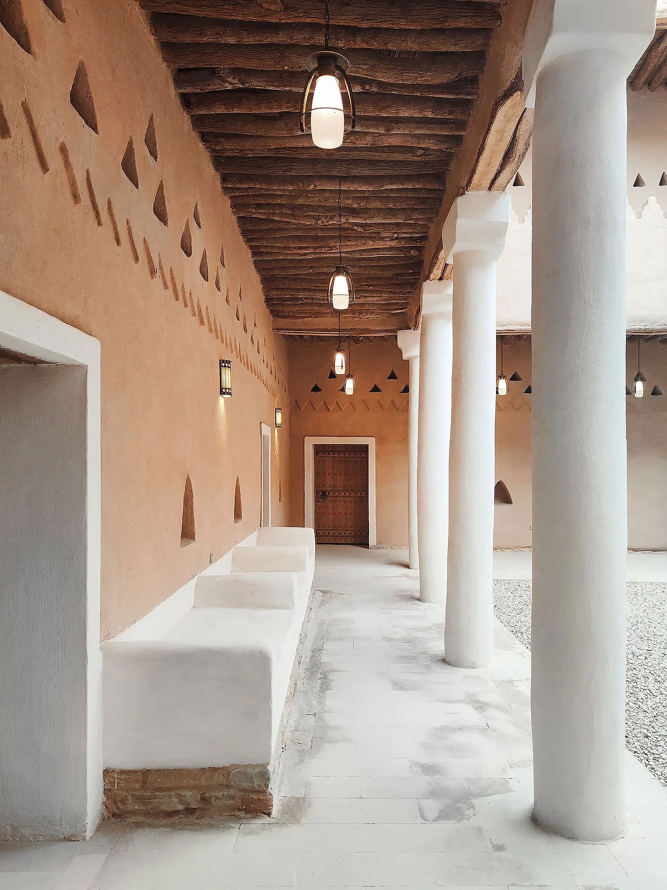 Masivní bílé sloupy, texturovanými hliněnými stěnami a stropem z dřevěných trámů.
