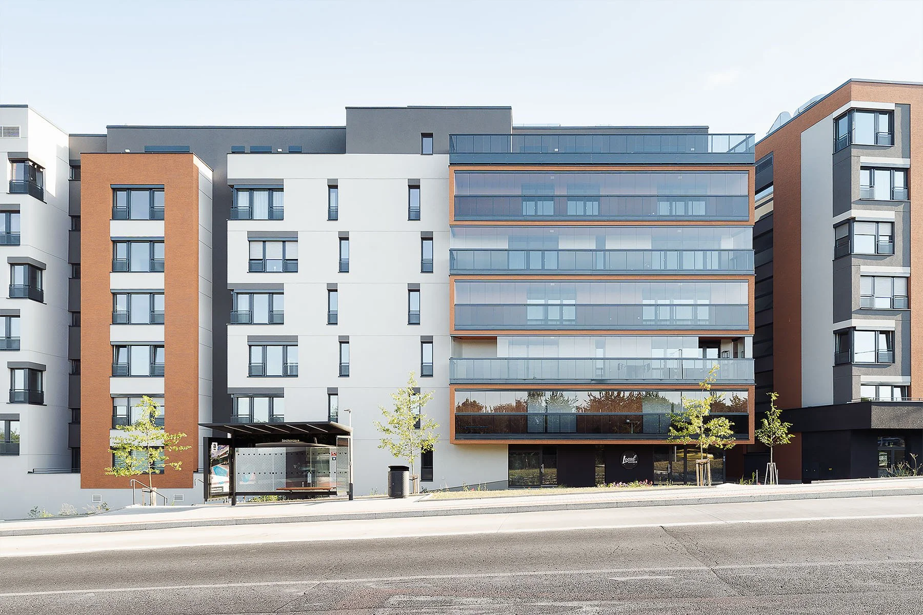 Moderní architektura bytového komplexu s prosklenými balkony a čistou fasádou u městské ulice.