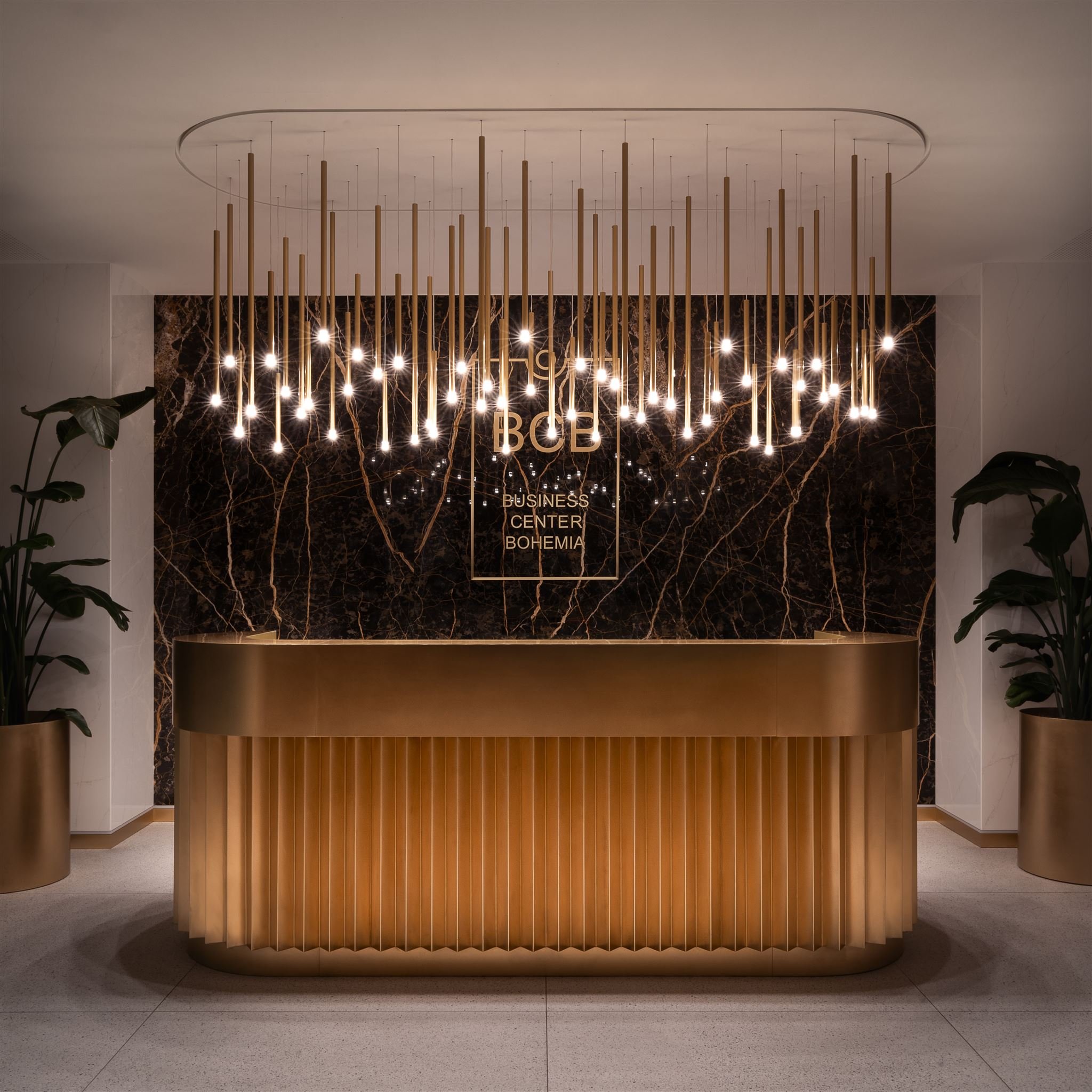 Elegantní recepce lobby s moderním lustrem, zlatým pultem a mramorovou stěnou.