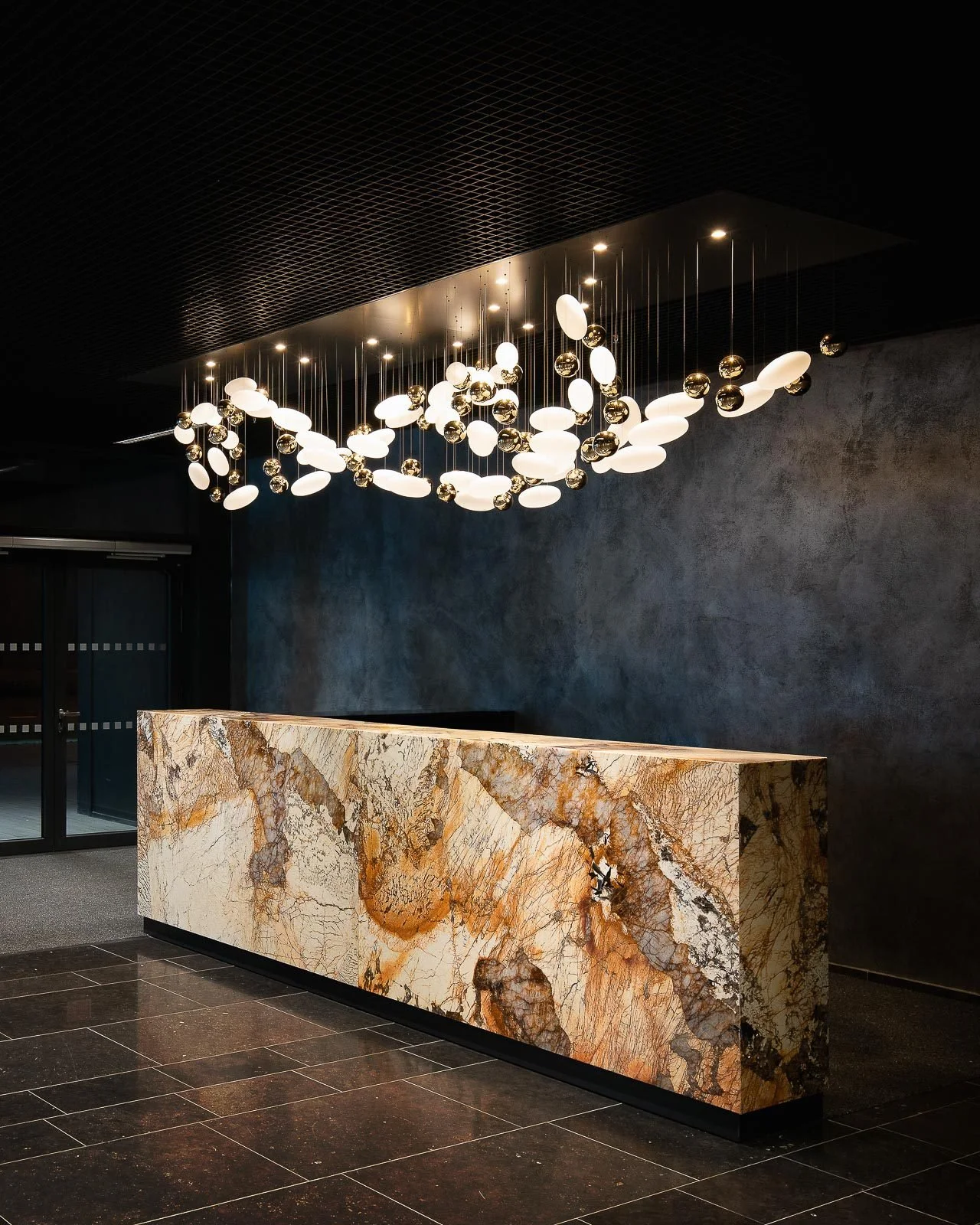 Elegantní recepce hotelu s mramorovým pultem a skleněnými designovými svítidly.