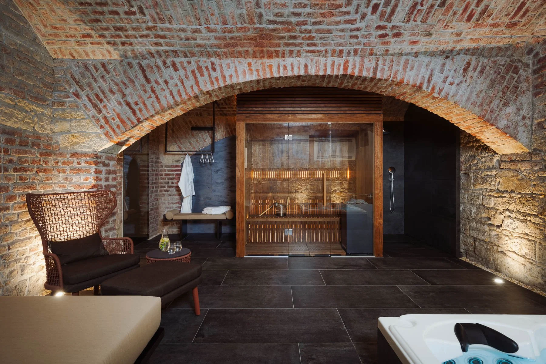 Moderní wellness zázemí s dřevěnou saunou, černou sprchou, vířivkou a lehátkem v elegantním interiéru.