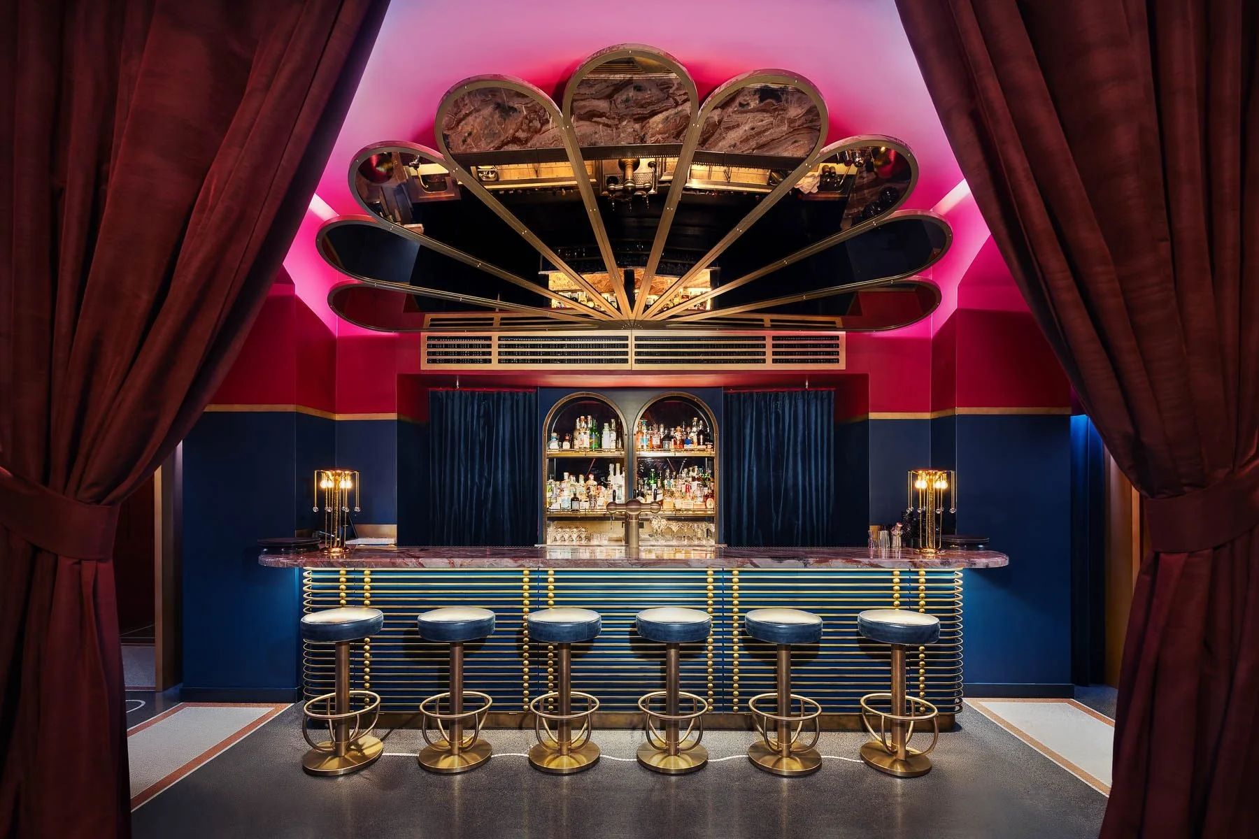 Luxusní barový interiér hotelu W Prague s námořnickou modří, zlatými detaily a unikátním stropním svítidlem ve tvaru květu.
