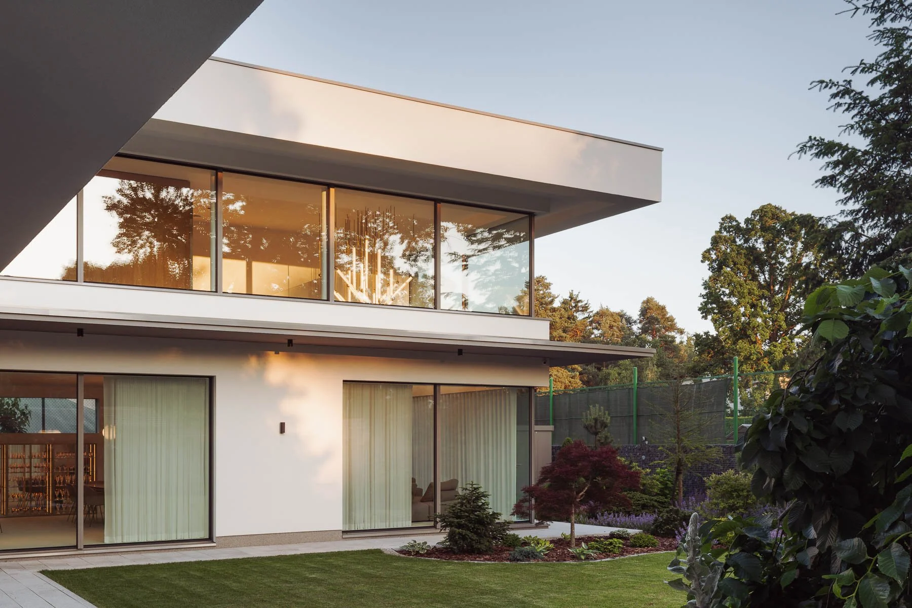 Architektura moderní vily s prosklenou fasádou a terasou propojující dům se zahradou.