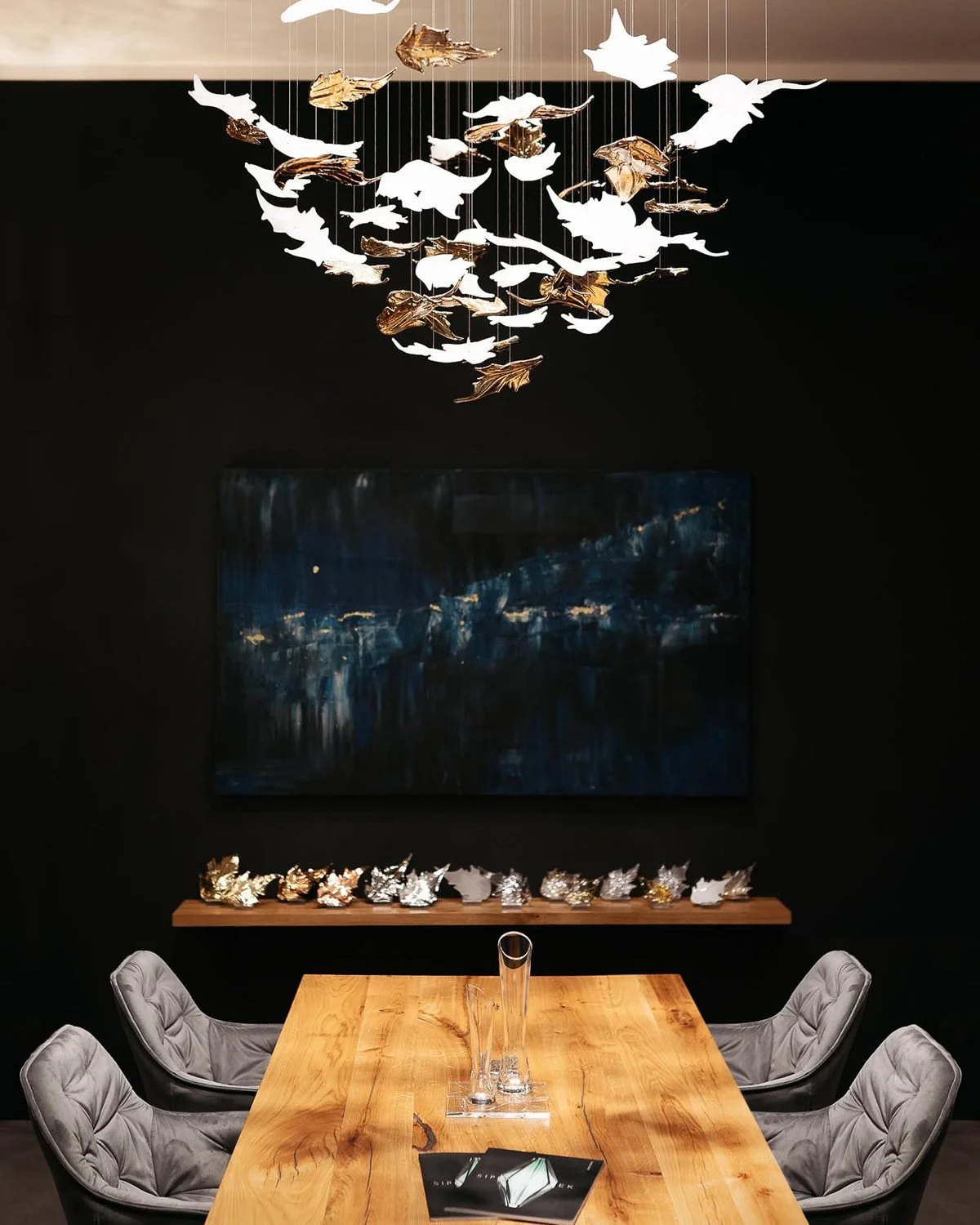 Moderní designový interiér s dřevěným stolem, šedými židlemi a luxusním svítidlem se skleněnými listy.