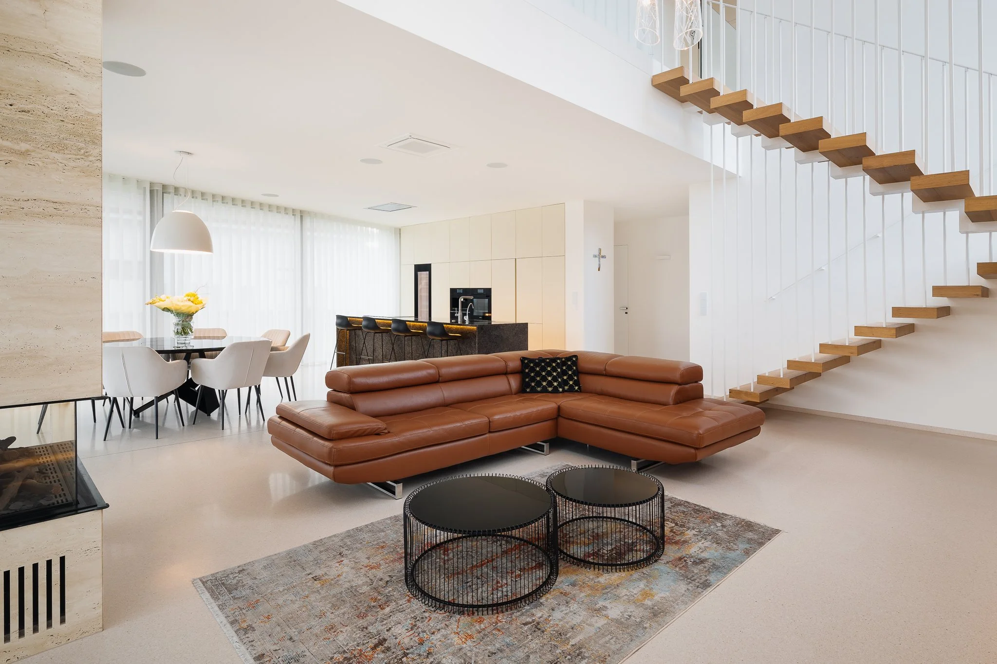 Vzdušný interiér obývacího pokoje s hnědou koženou sedačkou a monumentálním schodištěm.