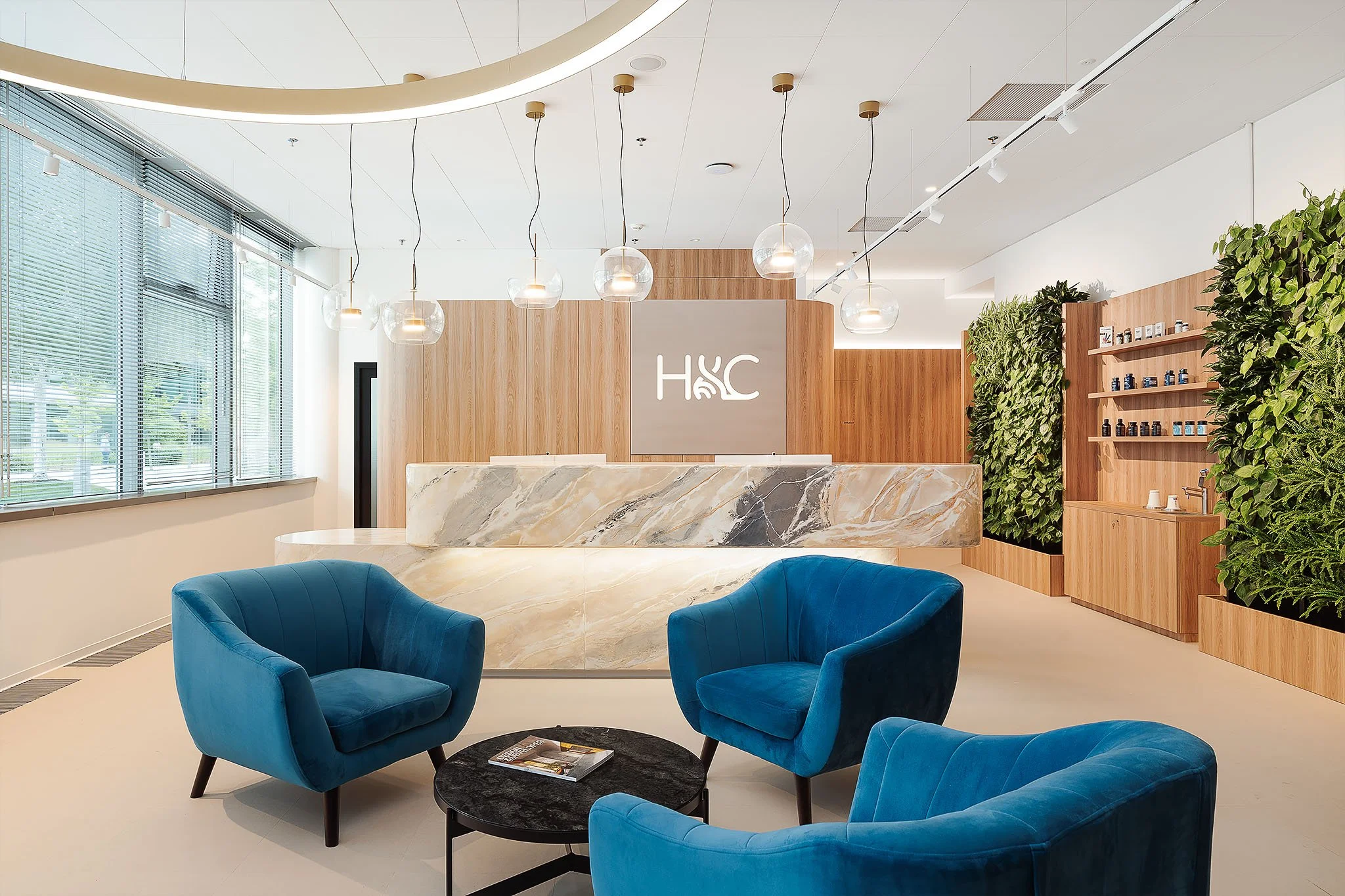 Interiér komerční recepce s modrými křesly, logem H&C a vertikální zahradou.