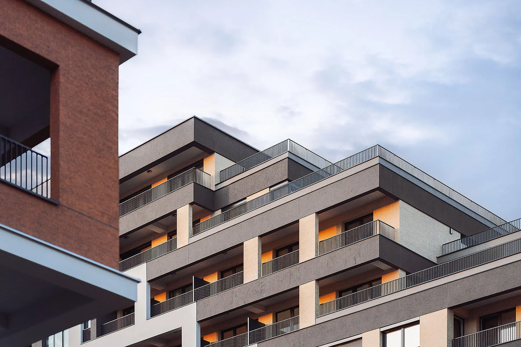 Geometrický detail architektury bytového domu s terasovitým uspořádáním a tmavou fasádou.