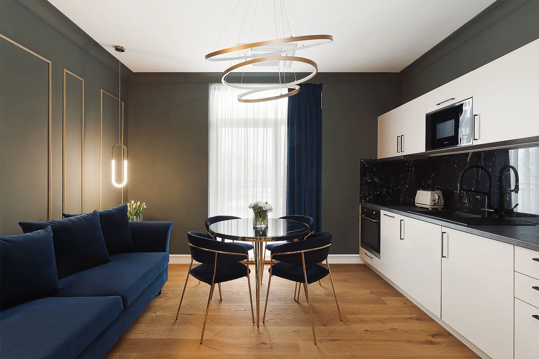 Záběr na tmavší interiér jídelny a kuchyně s moderním osvětlením.