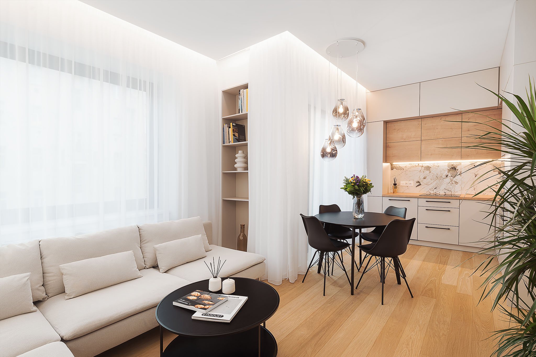 Moderní interiér otevřeného obývacího pokoje s černým jídelním stolem a světlou kuchyňskou linkou.