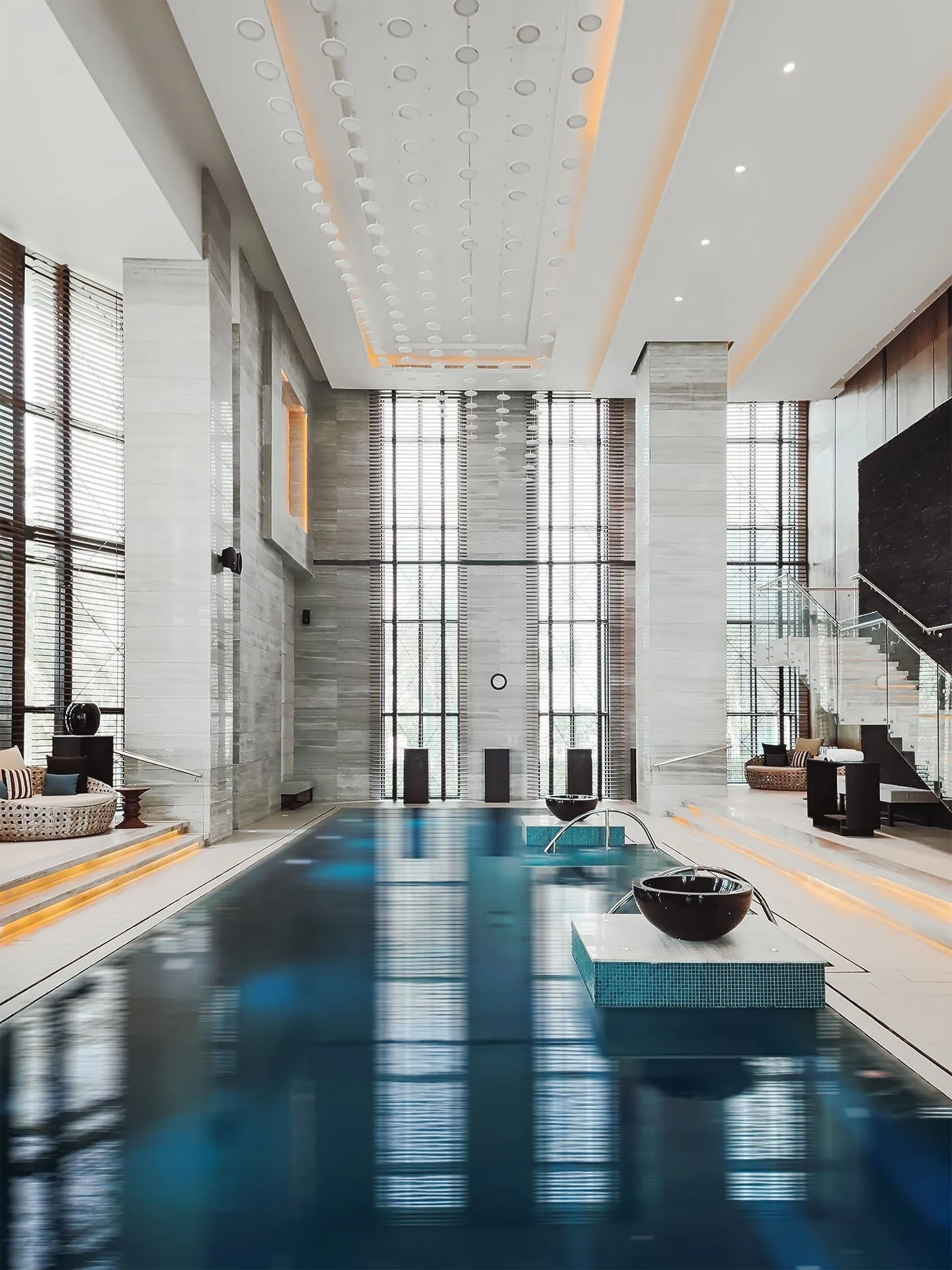 Architektonická fotografie vnitřního bazénu v hotelu Fairmont Riyadh: luxusní wellness prostor s monumentálními sloupy, ambientním podsvícením stropu a symetrickým moderním designem v Saúdské Arábii.