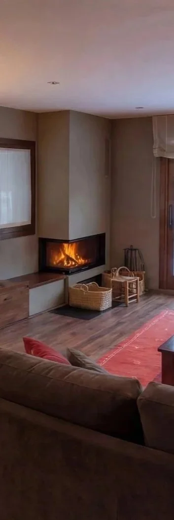 Detalle de Salón cálido con chimenea esquinera en proyecto de interiorismo para refugio de montaña en La Cerdanya. Diseño fluido con tonos arena y roble natural para una atmósfera de desconexión.