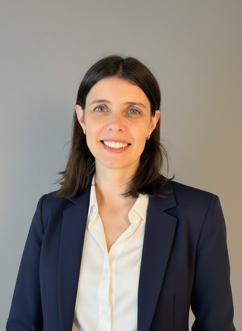 Retrato de una mujer con blusa blanca y blazer azul, sonriendo, fondo gris liso.