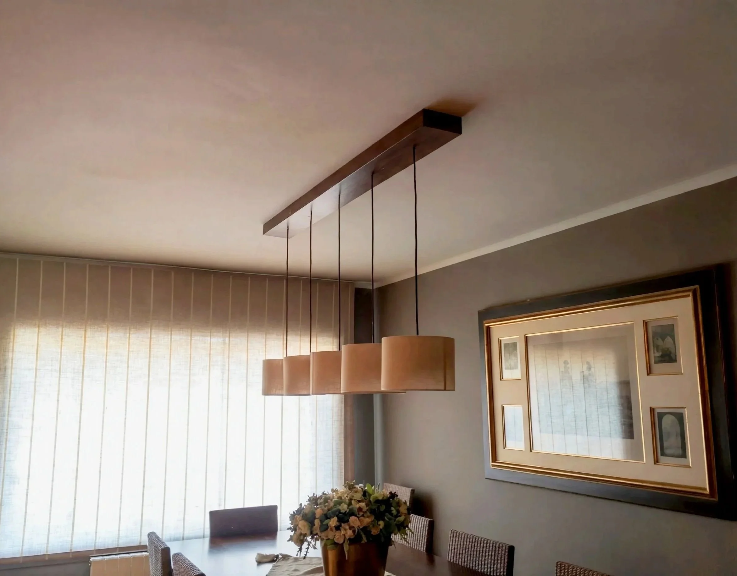 Comedor con mesa de madera y lámpara suspendida en reforma integral en La Cerdanya. Sustitución de acabados pesados por una paleta orgánica que amplía visualmente el espacio.