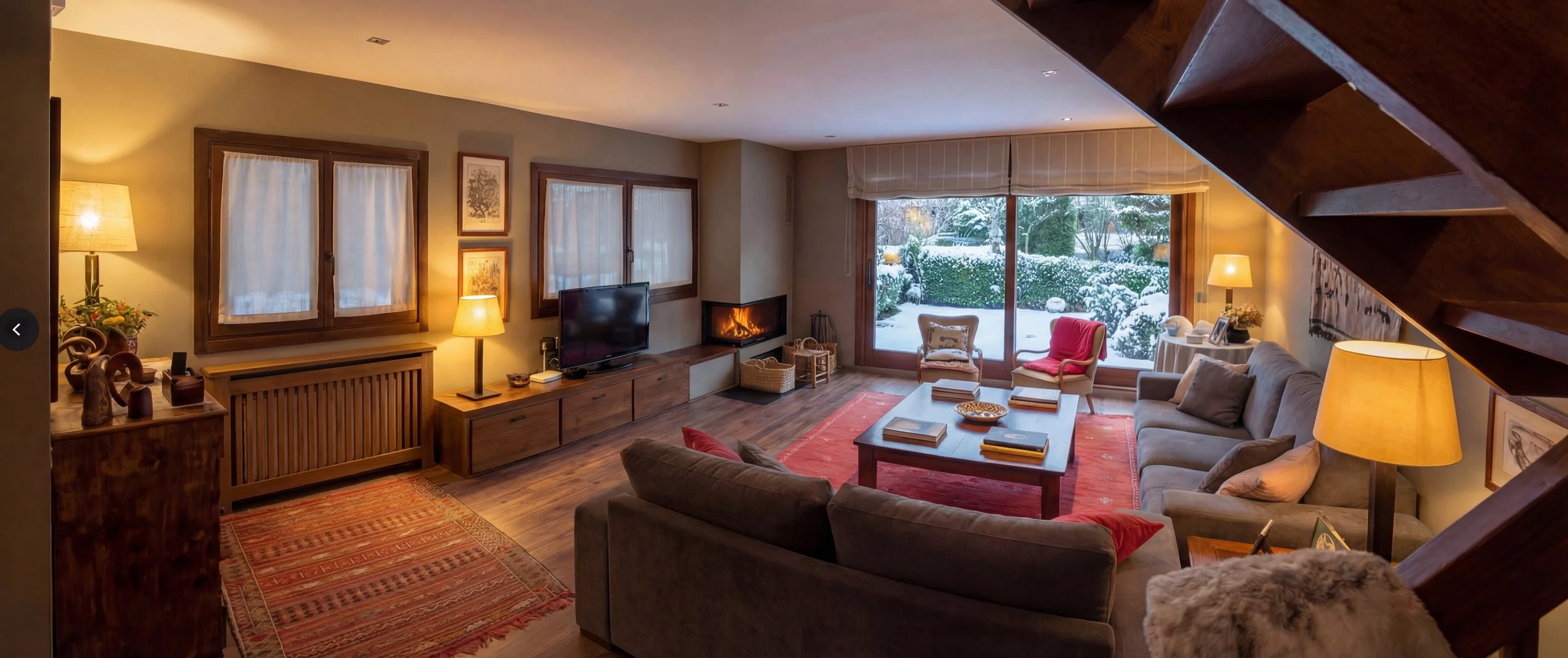 Salón cálido con chimenea esquinera en proyecto de interiorismo para refugio de montaña en La Cerdanya. Diseño fluido con tonos arena y roble natural para una atmósfera de desconexión.