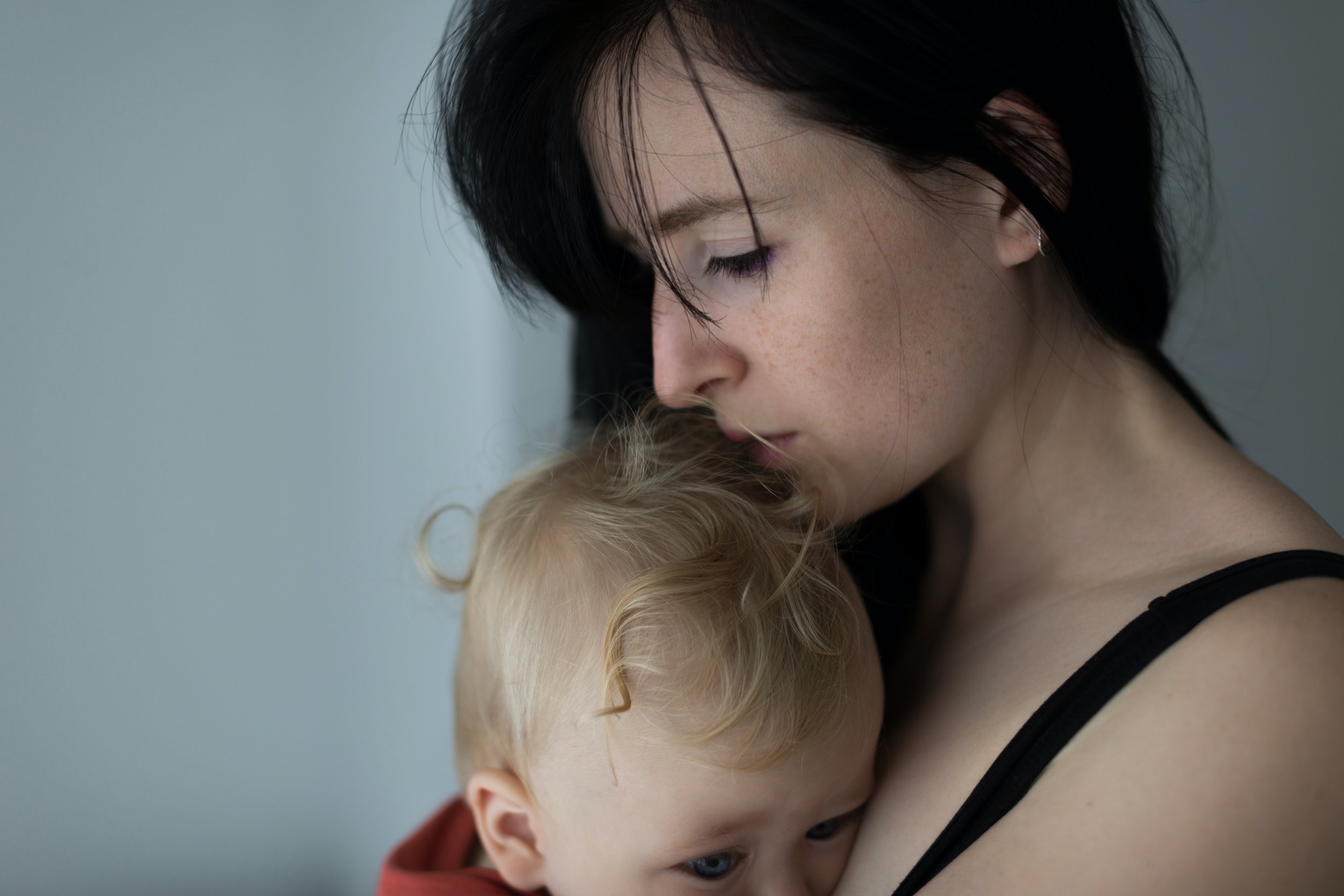 A woman with dark hair and earrings is hugging a young boy with blond hair and blue eyes, both with their eyes closed.