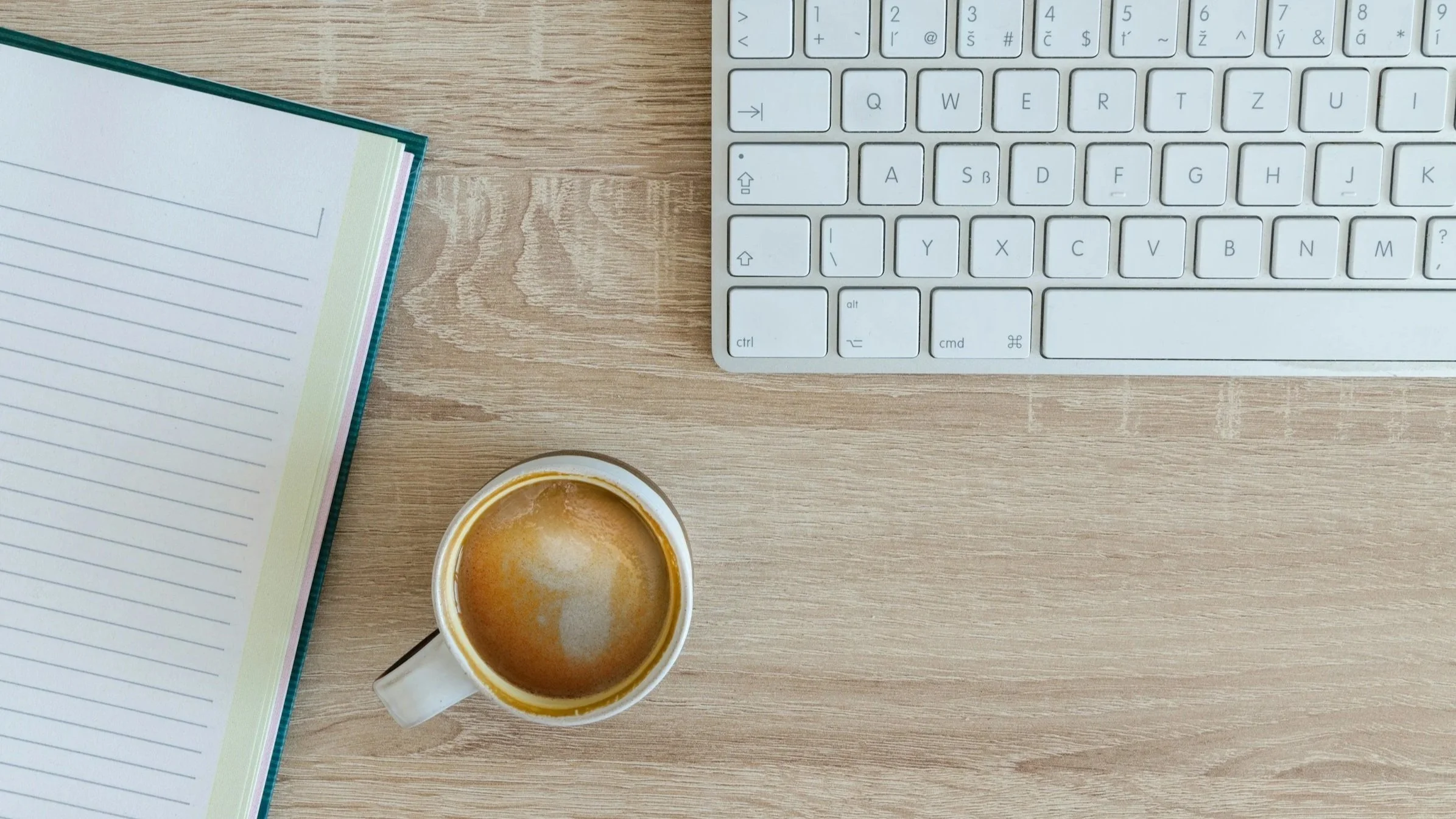 A workspace with a notebook, a keyboard, and a cup of coffee on a wooden desk.