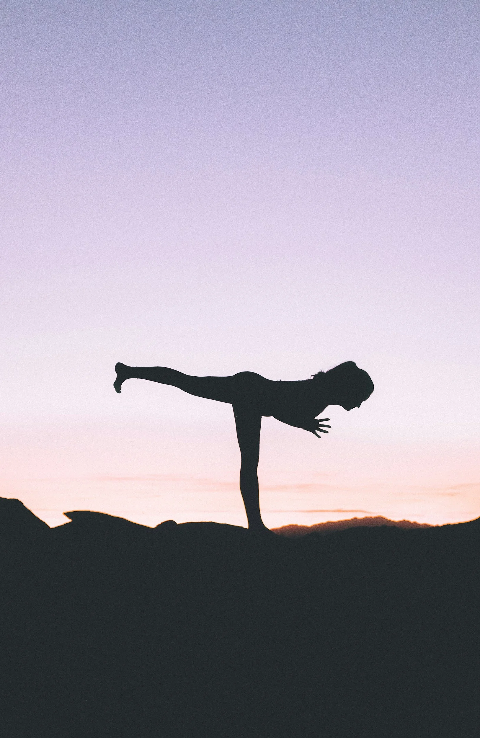 Silhouette of a woman performing a yoga pose on a rocky terrain during sunset or sunrise.