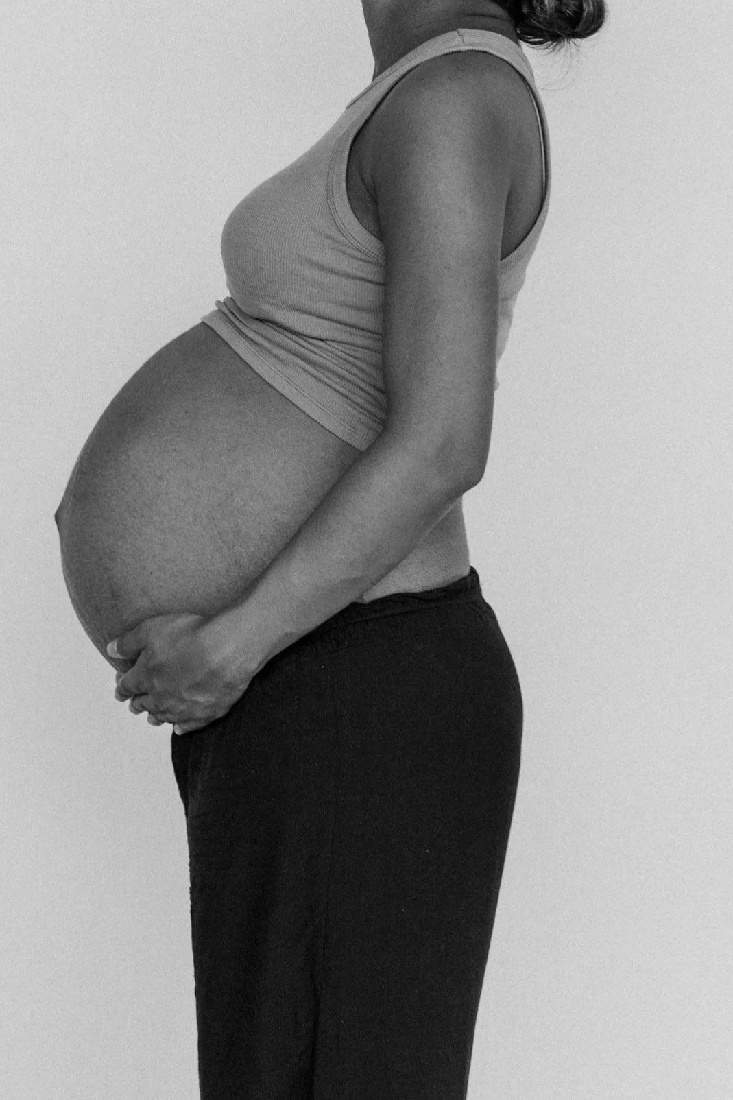 Side view of a pregnant woman holding her belly, in grayscale.