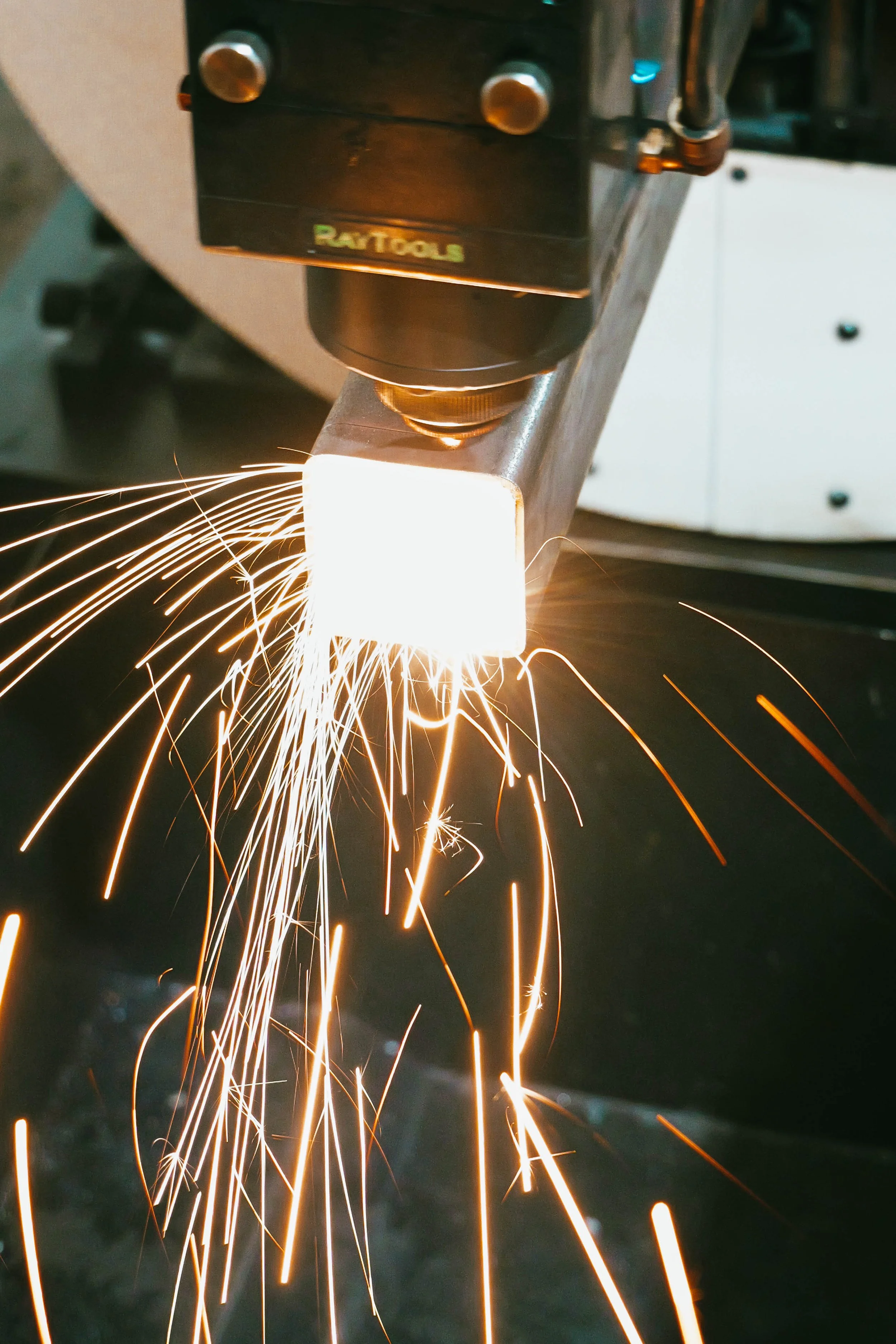 A welding machine welds a metal piece, producing sparks and bright light.