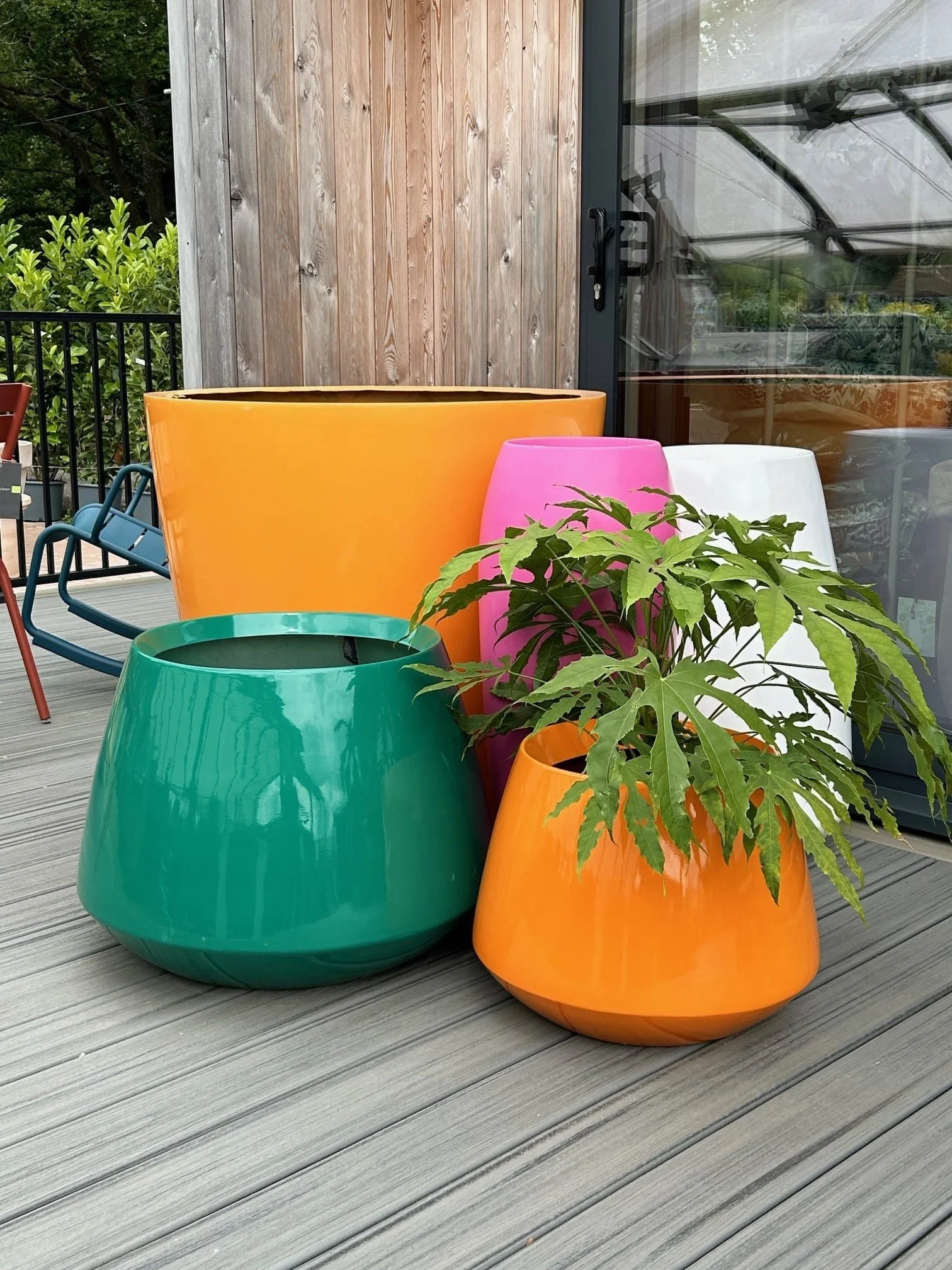 Colorful outdoor planters in yellow, pink, white, green, and orange with a green leafy plant on a wooden patio.