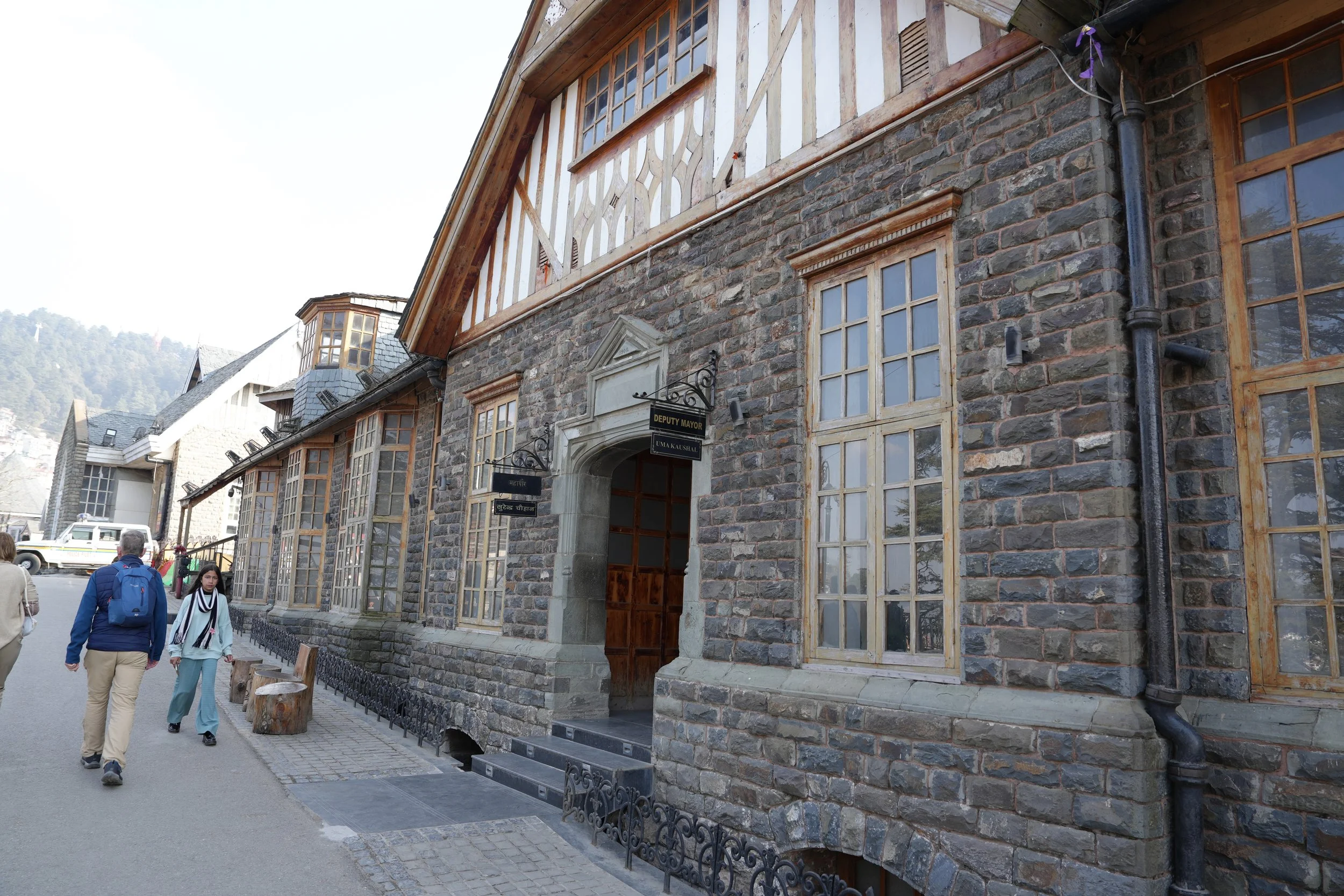  Stone and timber colonial-era building on Mall Road in Shimla, with tall windows, wooden beams, and pedestrians walking along the pavement in the cool mountain air. 