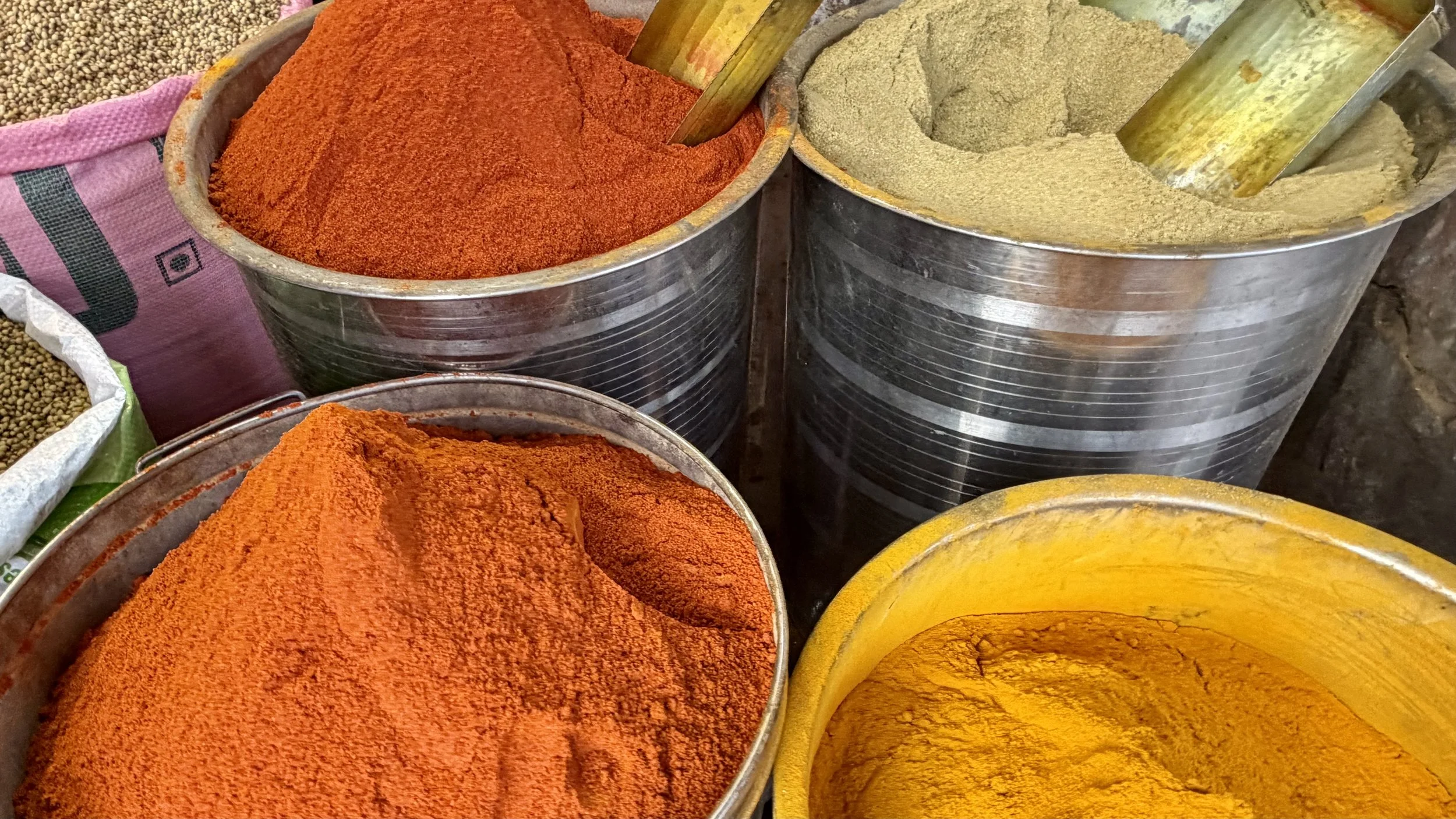 Metal tubs filled with mounds of ground spices in orange, yellow and pale beige at a Jaipur market stall.