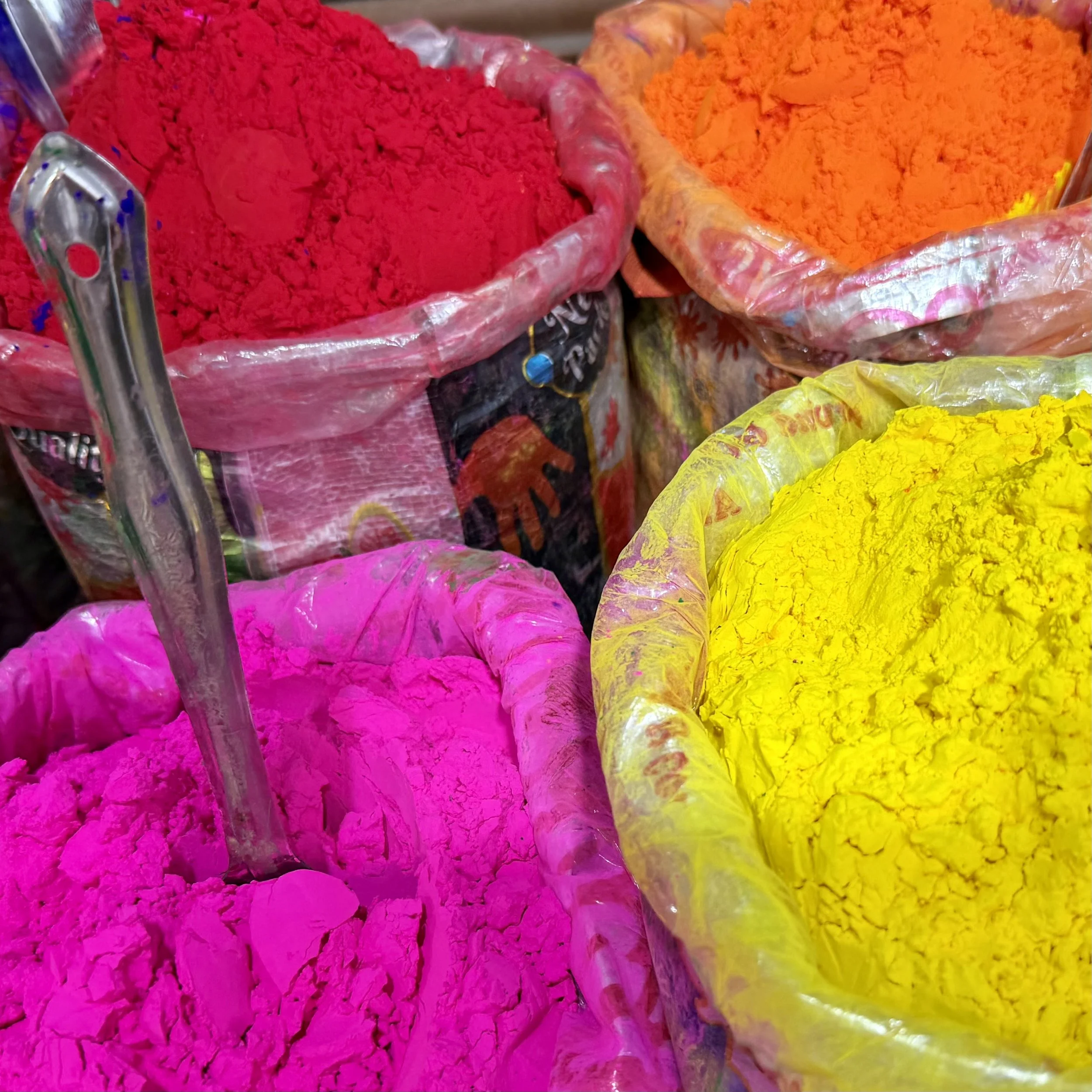 Bright pink, red, orange and yellow Holi powder piled in open tubs with metal scoops.