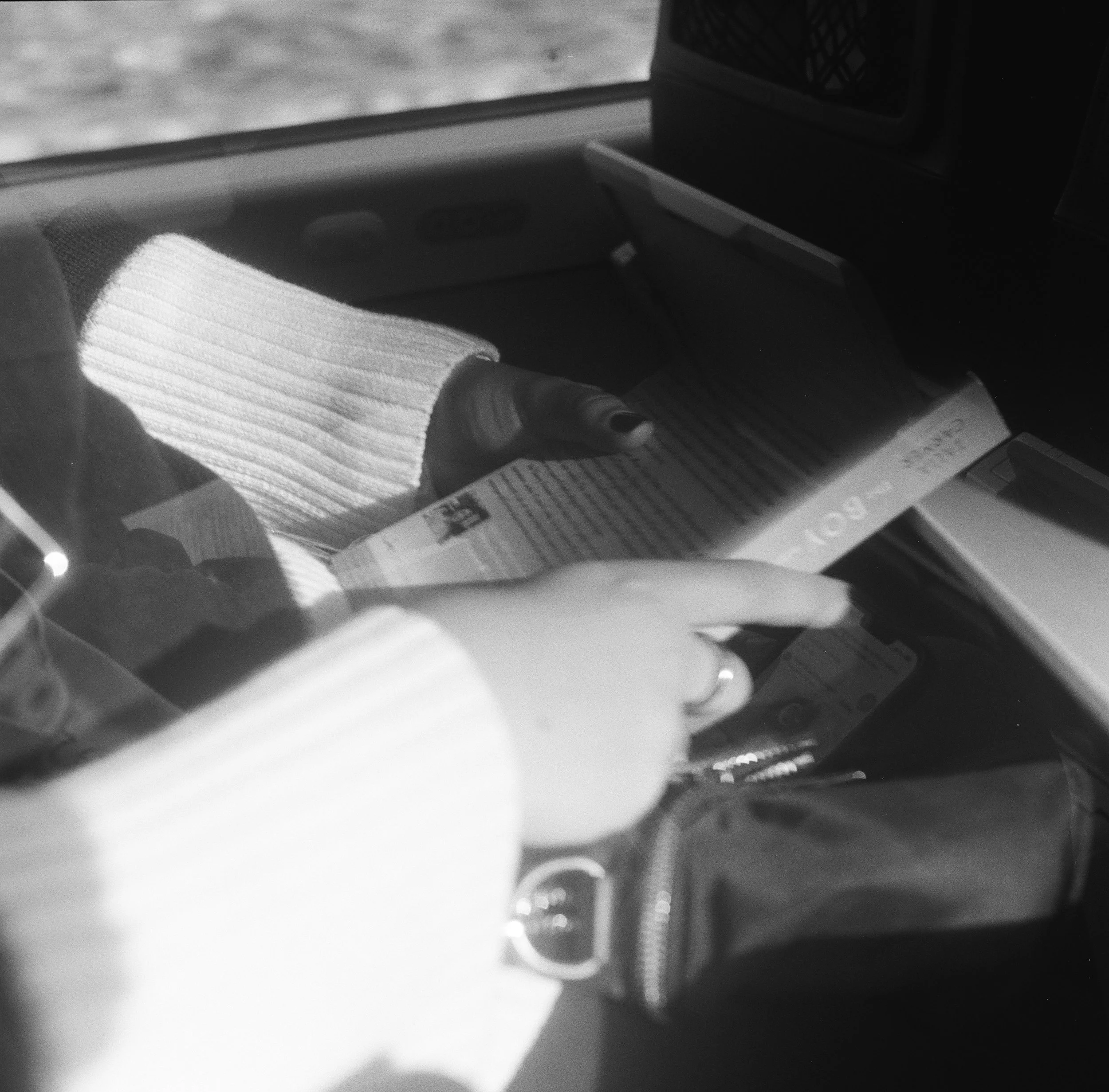 Close-up of a person reading a transit card or ticket, with a hand pointing at a device or screen, wearing a knitted sweater, inside a vehicle.