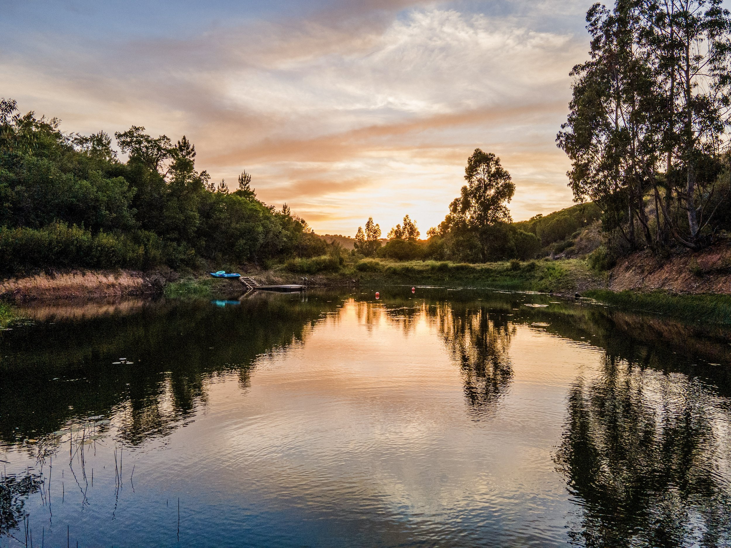 A peaceful river at sunset with calm water reflecting the colorful sky and trees on both sides.