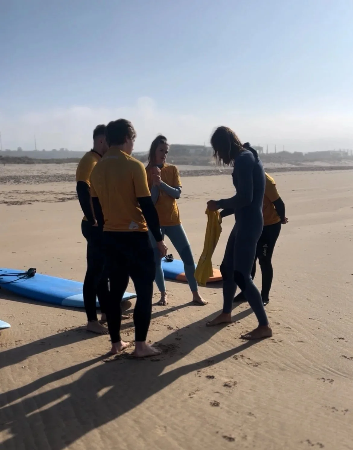 Tiago Madeira Surf Group of people on the beach preparing for surfing, with surfboards on the sand.