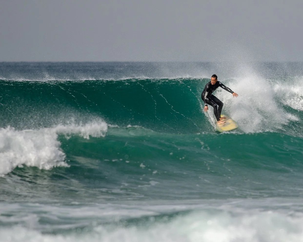 Tiago Madeira on a wave in the ocean, wearing a black wetsuit.
