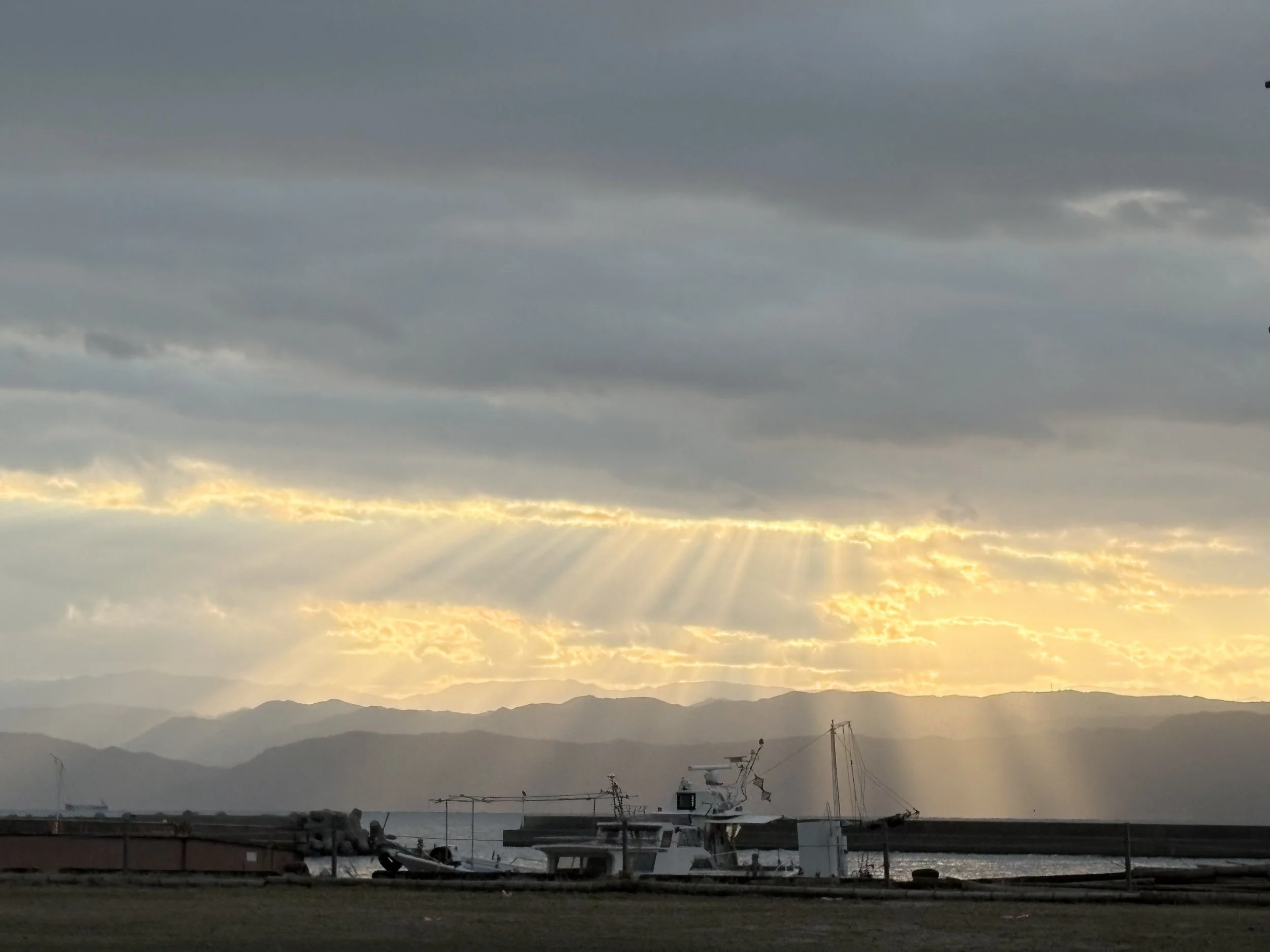 沈む夕日が海と山々を照らす、漁船が停泊している港の風景