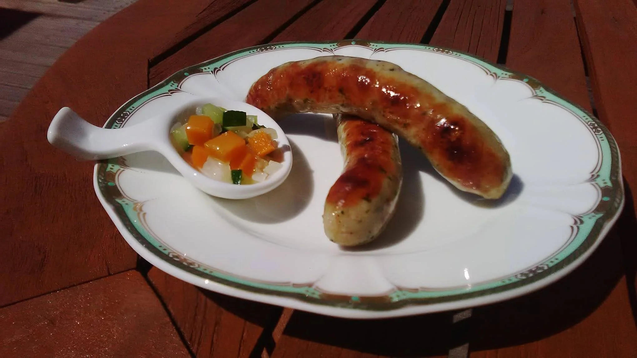 焼きソーセージと彩り野菜の付け合わせが載った白い皿、木製のテーブルの上に置かれている