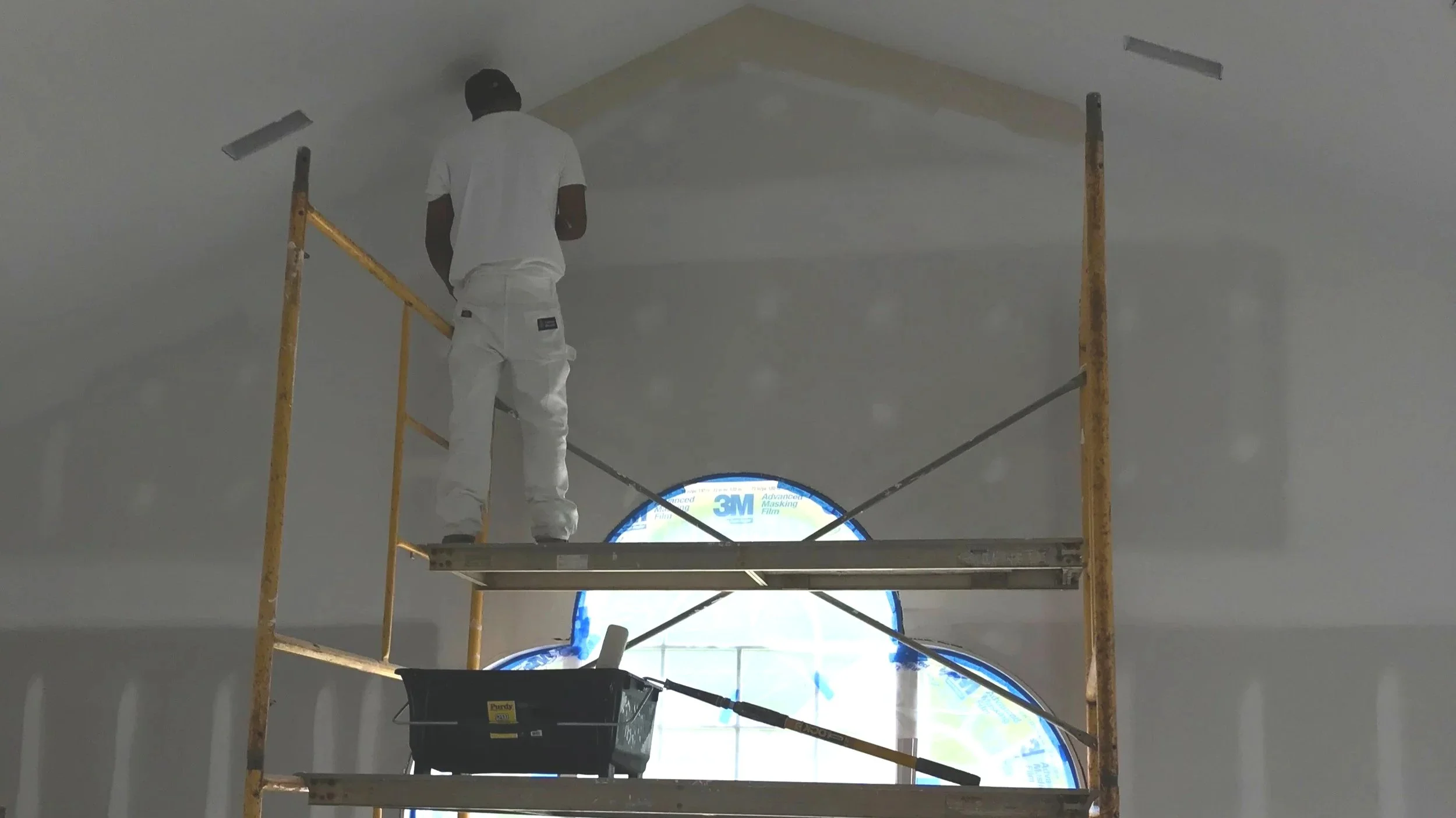Drywall installation on a high interior ceiling using scaffolding during a home renovation.