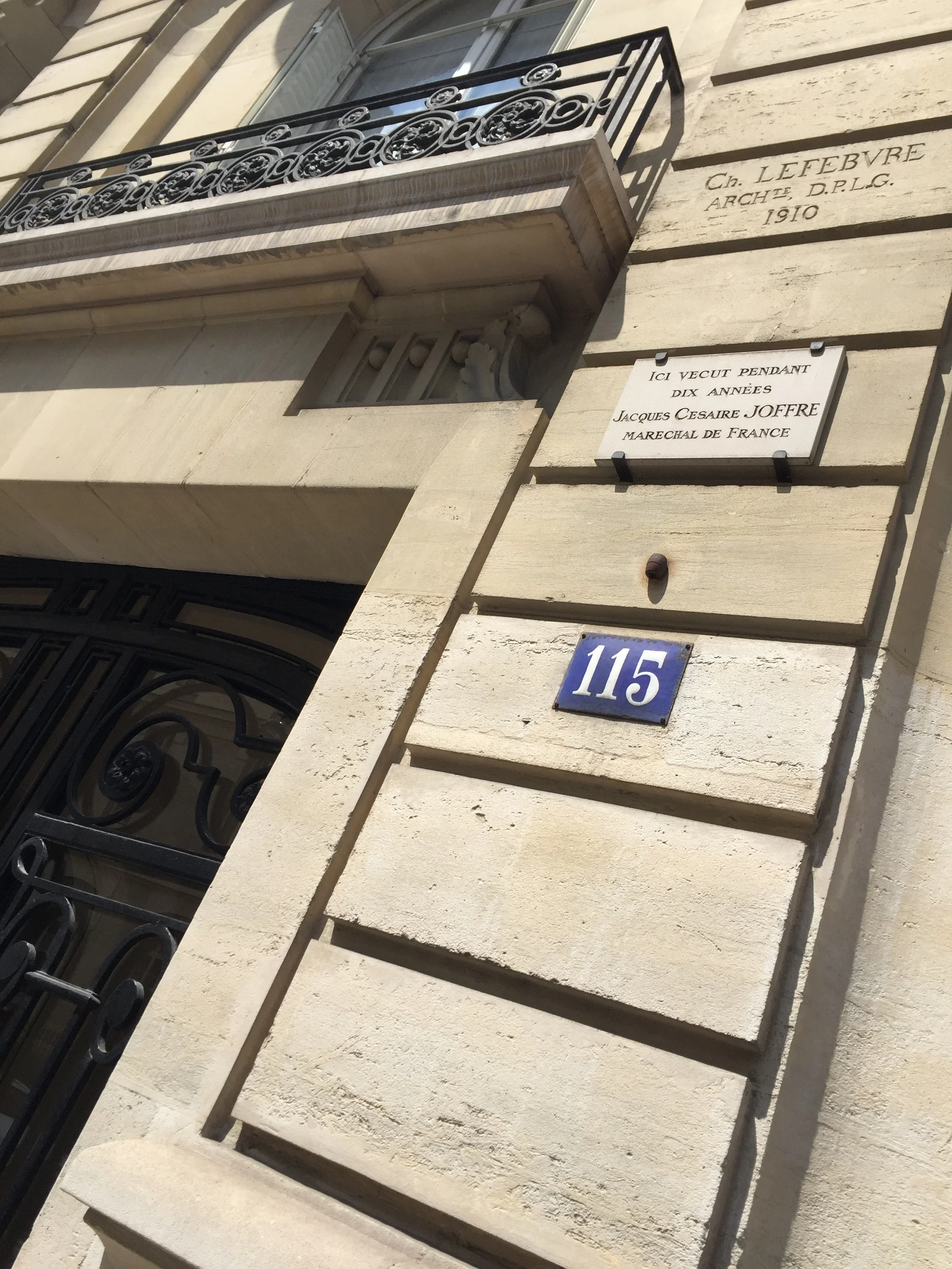 Façade d'un bâtiment avec un balcon en fer forgé, une plaque avec le nom Ch. Lefebvre et la date 1910, une plaque commémorative indiquant que Jacques Césaire Joffre a vécu ici pendant dix ans, et une plaque bleue portant le numéro 115.