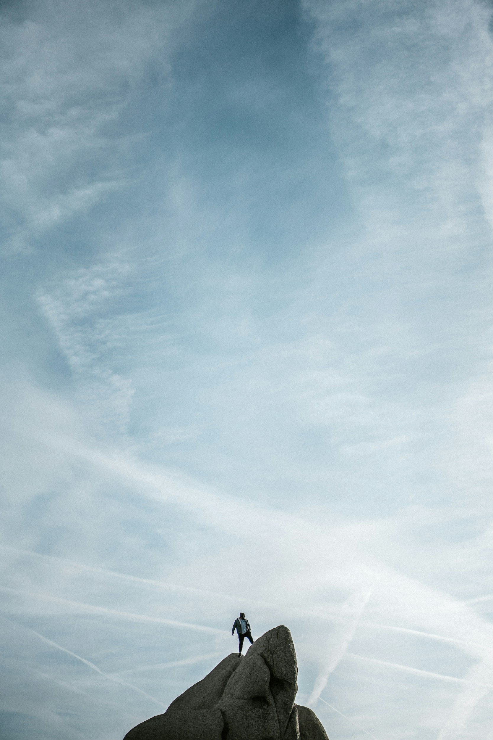 A person standing on top of a large rock formation outdoors under a wide sky with clouds.