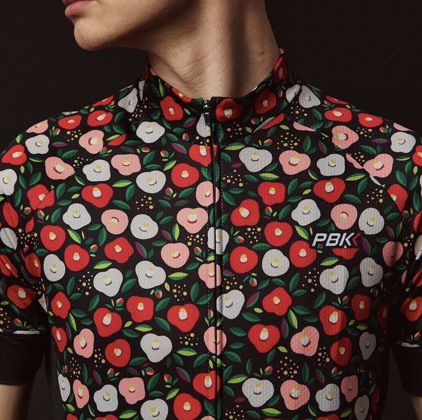 Close up image of a cyclist's chest wearing a jersey decorated with white and red poppies and a PBK logo on the right hand side of his chest.
