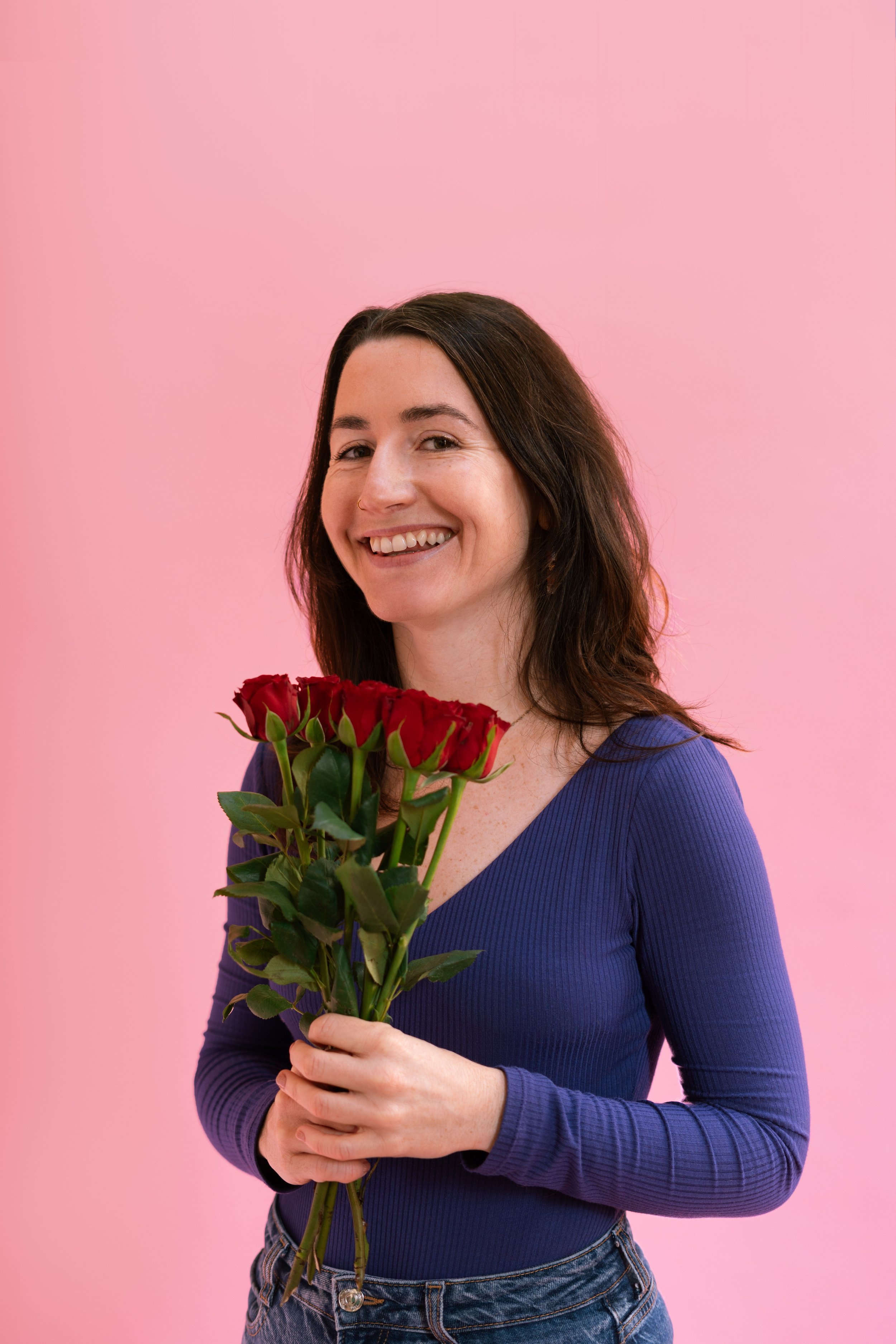 Femme souriante tenant un bouquet de roses rouges contre un fond rose
