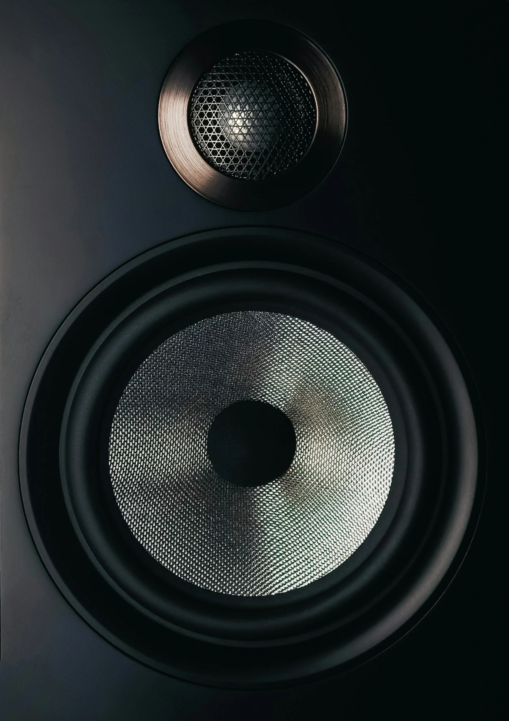 Close-up of a black speaker with a round metal grille in a dark setting.