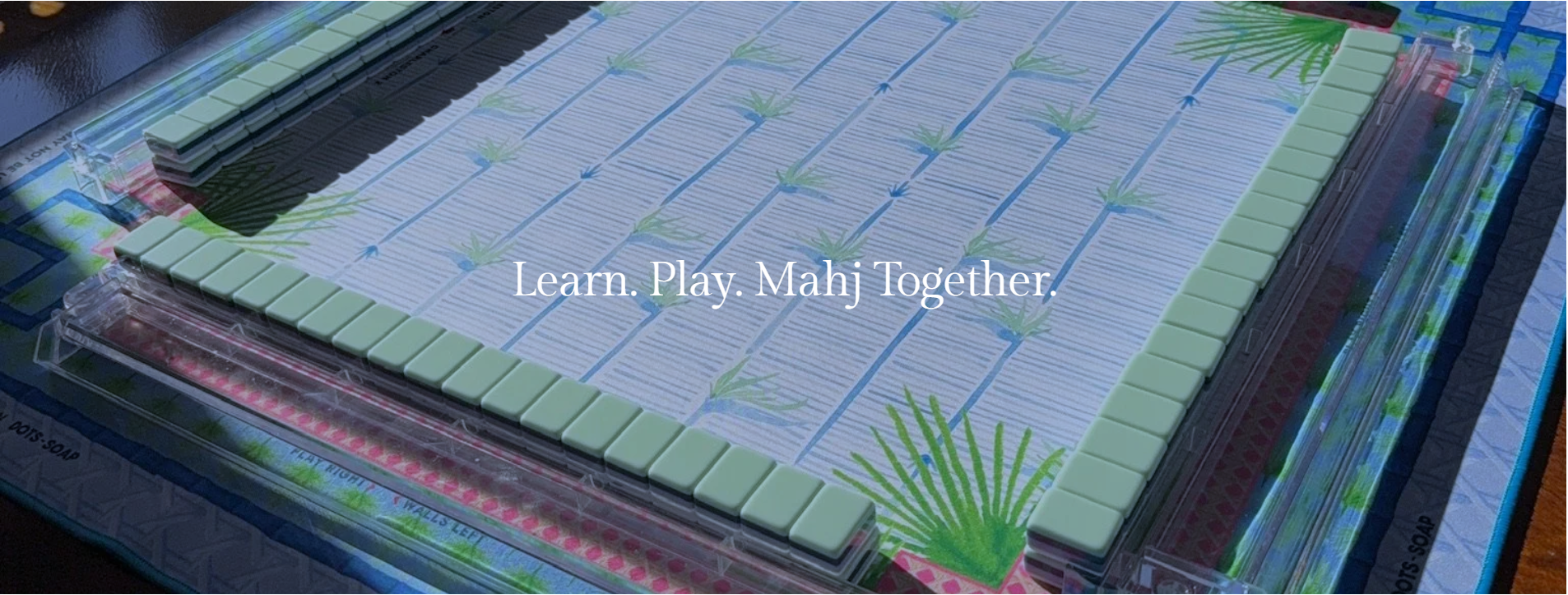 Close-up of a Mahjong game table with green tiles and a decorative mat, with the caption 'Learn. Play. Mahjong Together.'