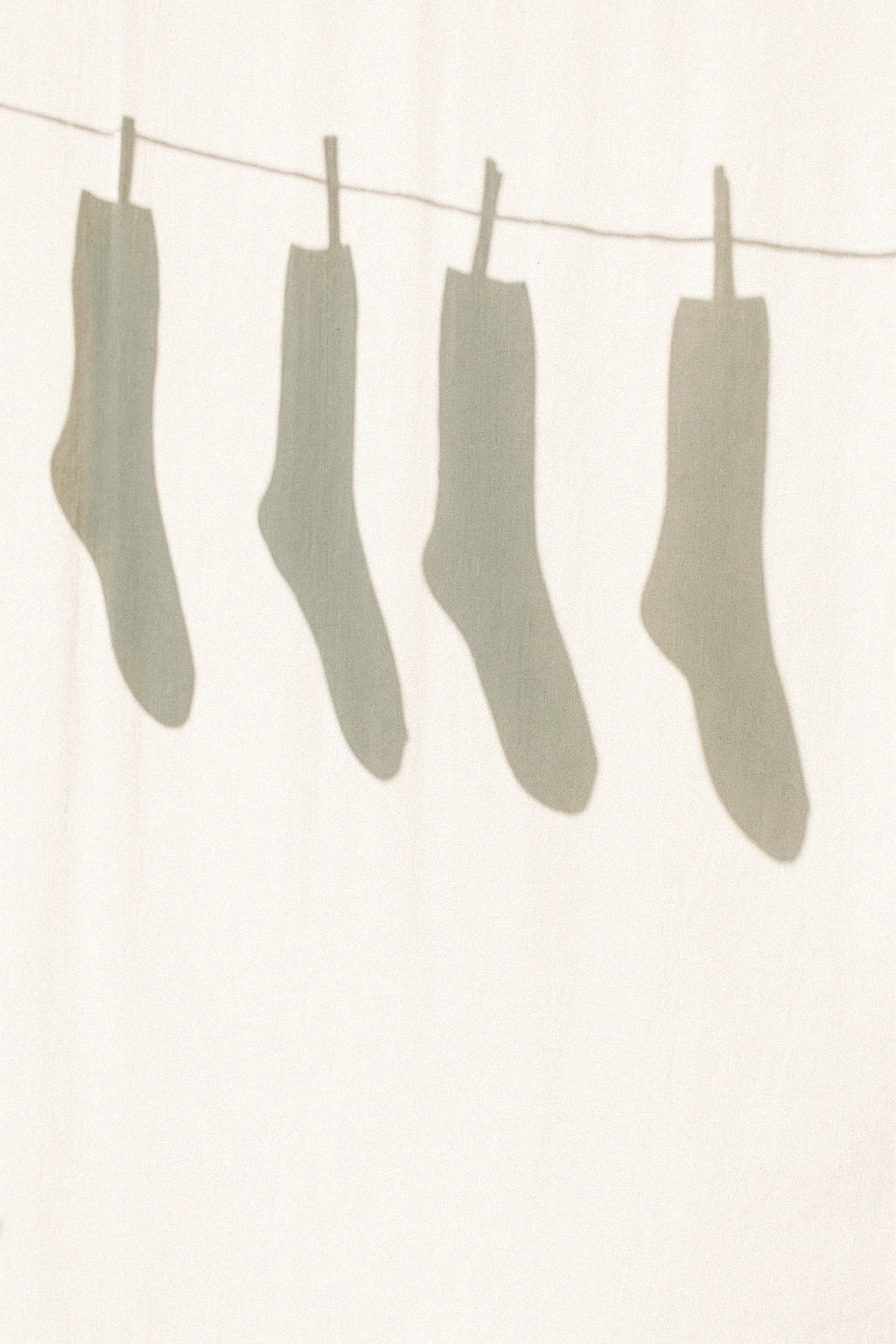 Four socks hanging on a clothesline with their shadows cast on the wall behind.