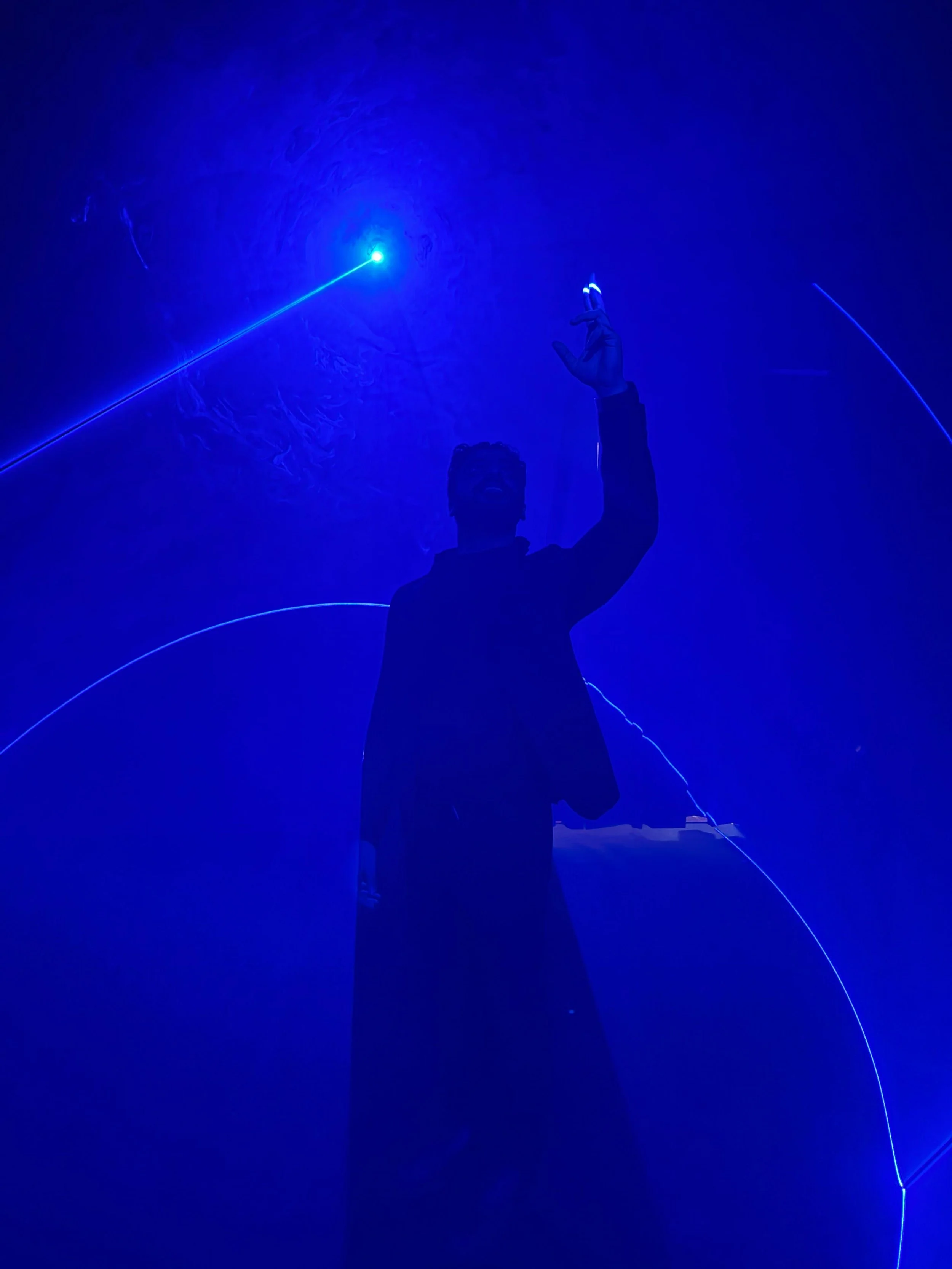 Moh'd Ghayeb silhouette against a blue background with laser light show and curved light streaks.