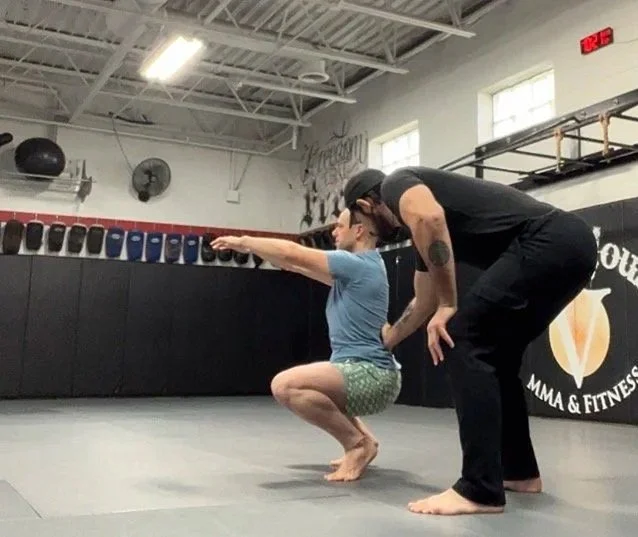 A man practicing a squat exercise with a trainer at a martial arts fitness gym.