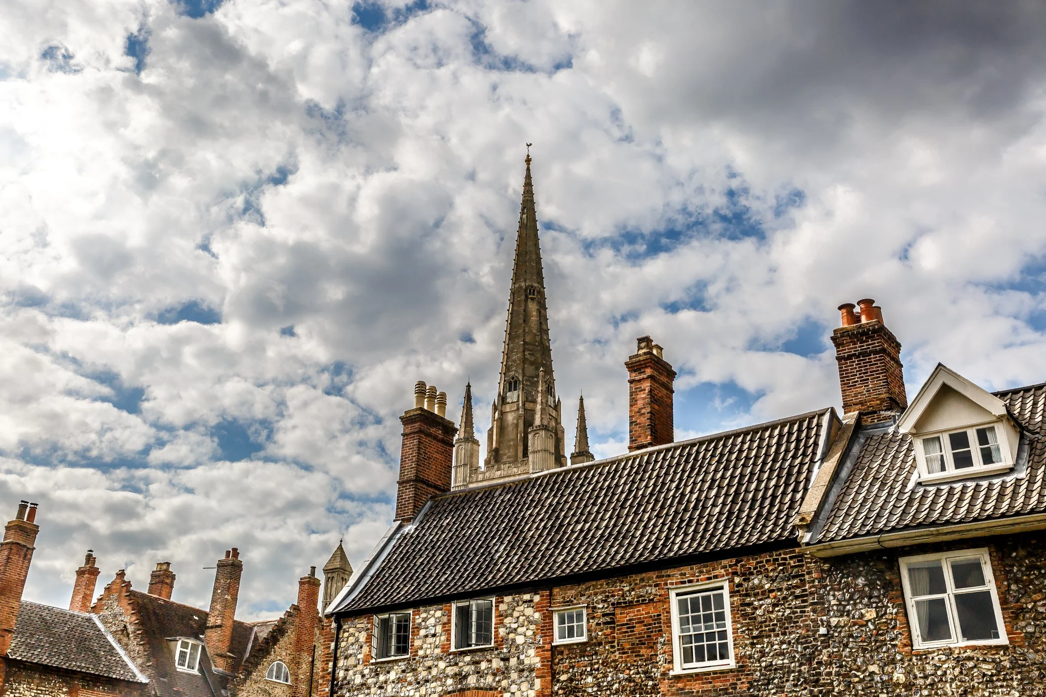 A view of old brick houses with a tall church steeple against a cloudy sky.