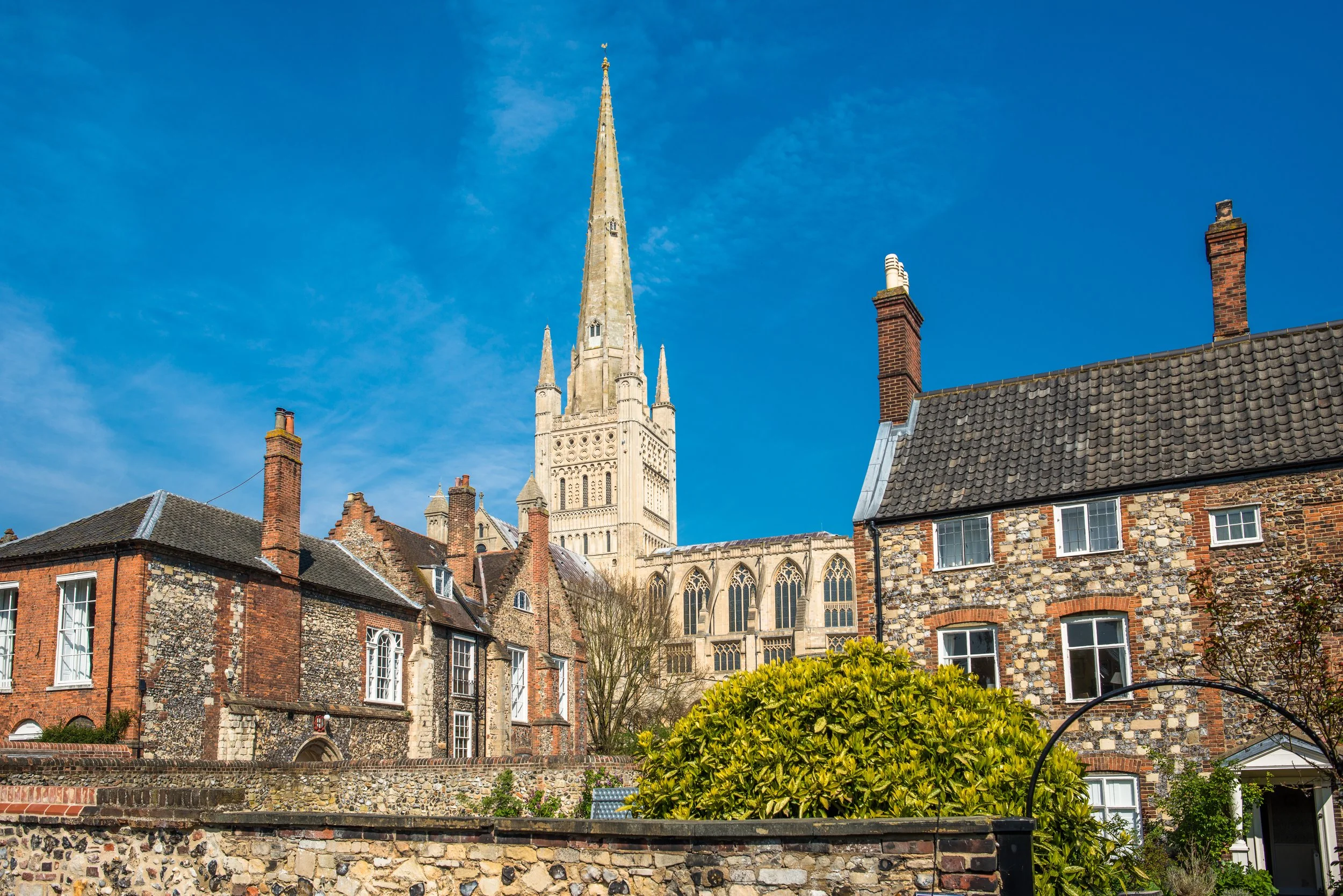 View of old residential houses with a large church or cathedral with a tall steeple in the background under a blue sky.