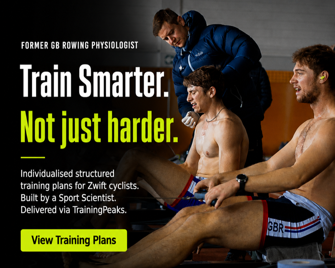 Two male cyclists receiving training advice from a coach in a gym setting. One cyclist is shirtless, sitting on a rowing machine, and the other cyclist is sitting beside him. Both are wearing cycling shorts, and the coach is standing behind them, leaning over and speaking.