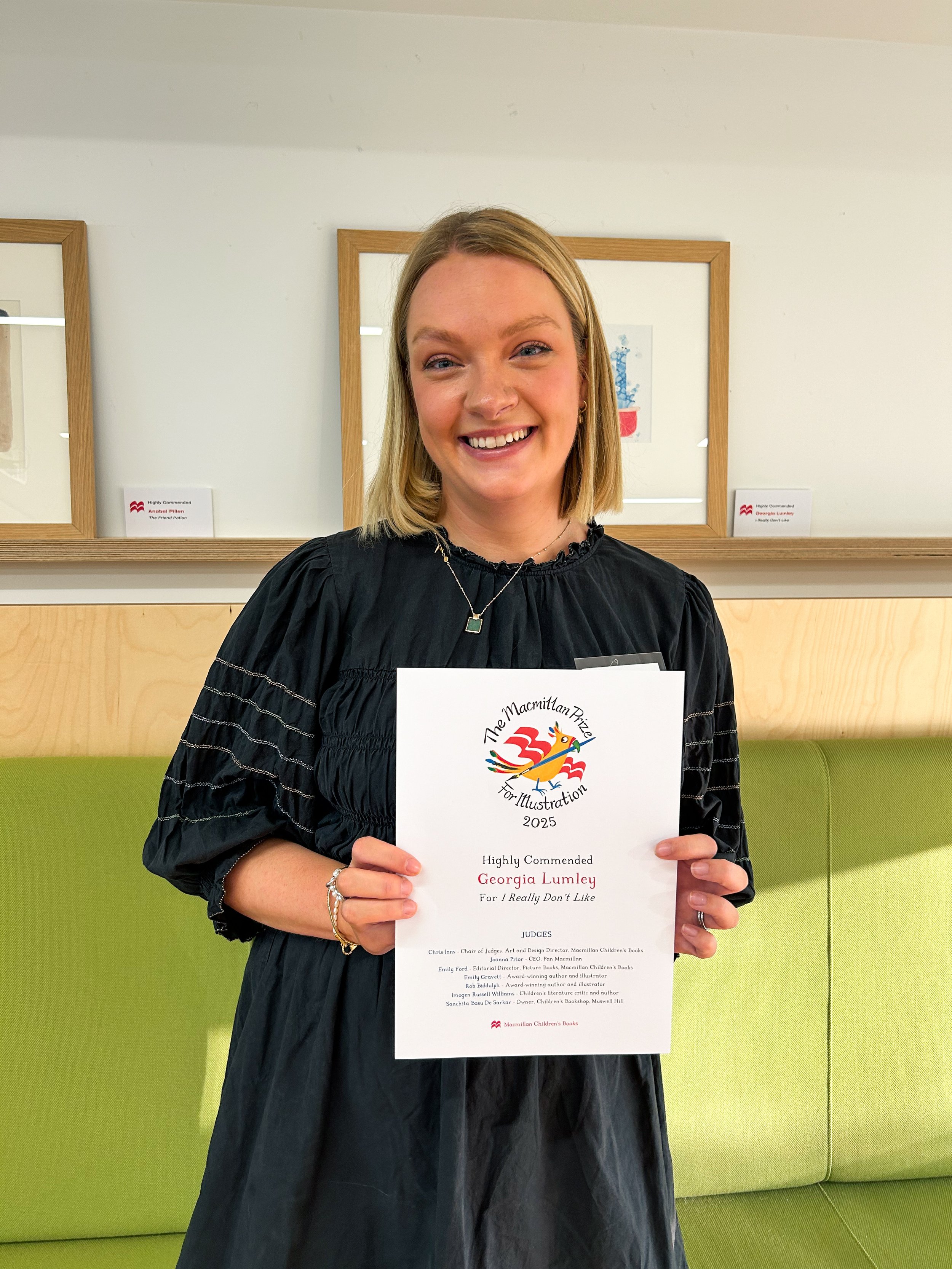 Georgia holding her certificate from the Macmillan Prize for Illustration 2025.