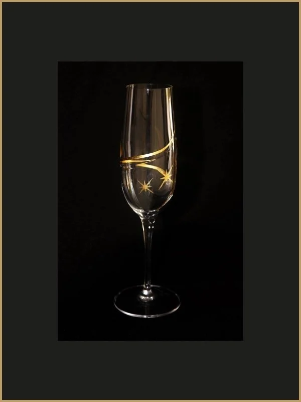 Verre de champagne avec décor doré, placé contre un fond noir.